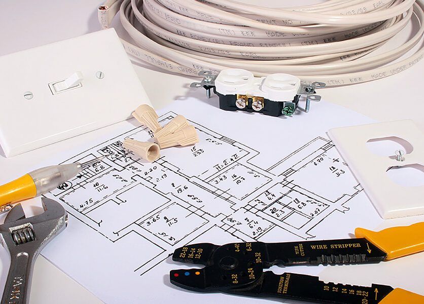 A wrench and pliers sit on top of a drawing of an electrical system