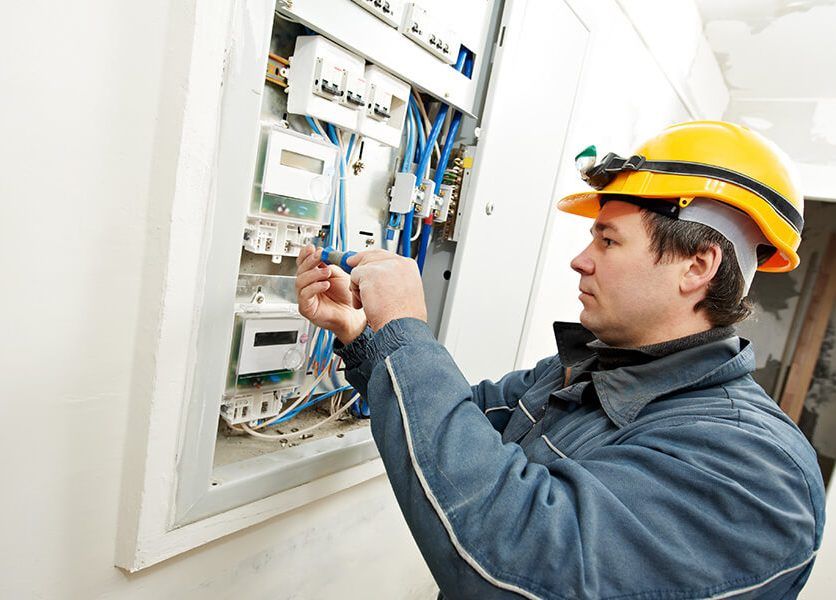 A man wearing a hard hat is working on an electrical box.
