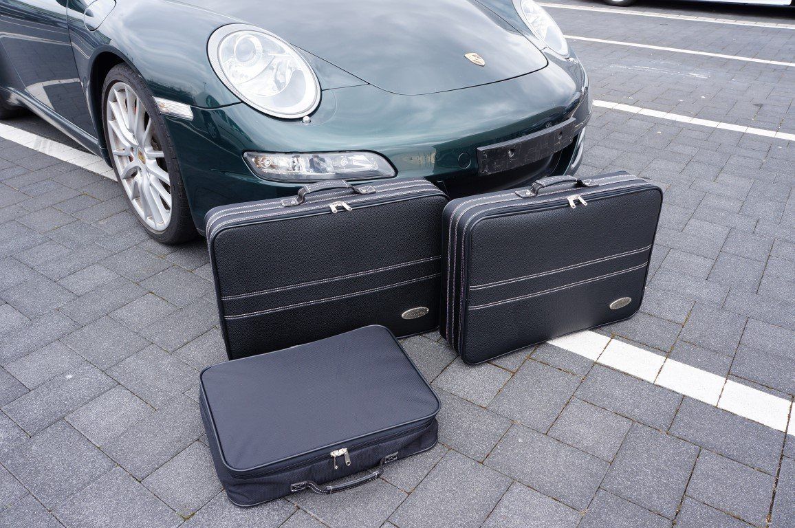 Een groene Porsche 911 staat geparkeerd op een parkeerplaats met drie koffers ervoor.
