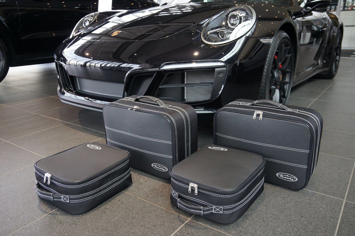 Een zwarte Porsche 911 staat geparkeerd in een showroom naast een set bagagetassen.