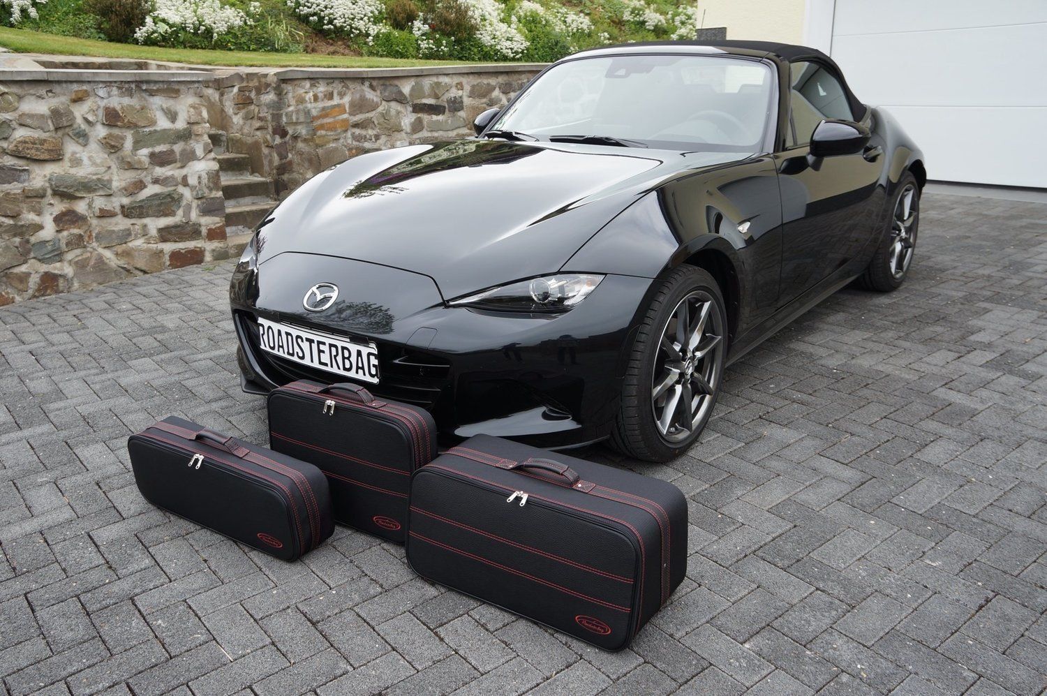 Een zwarte sportwagen staat geparkeerd op een bakstenen oprit naast een stenen muur.