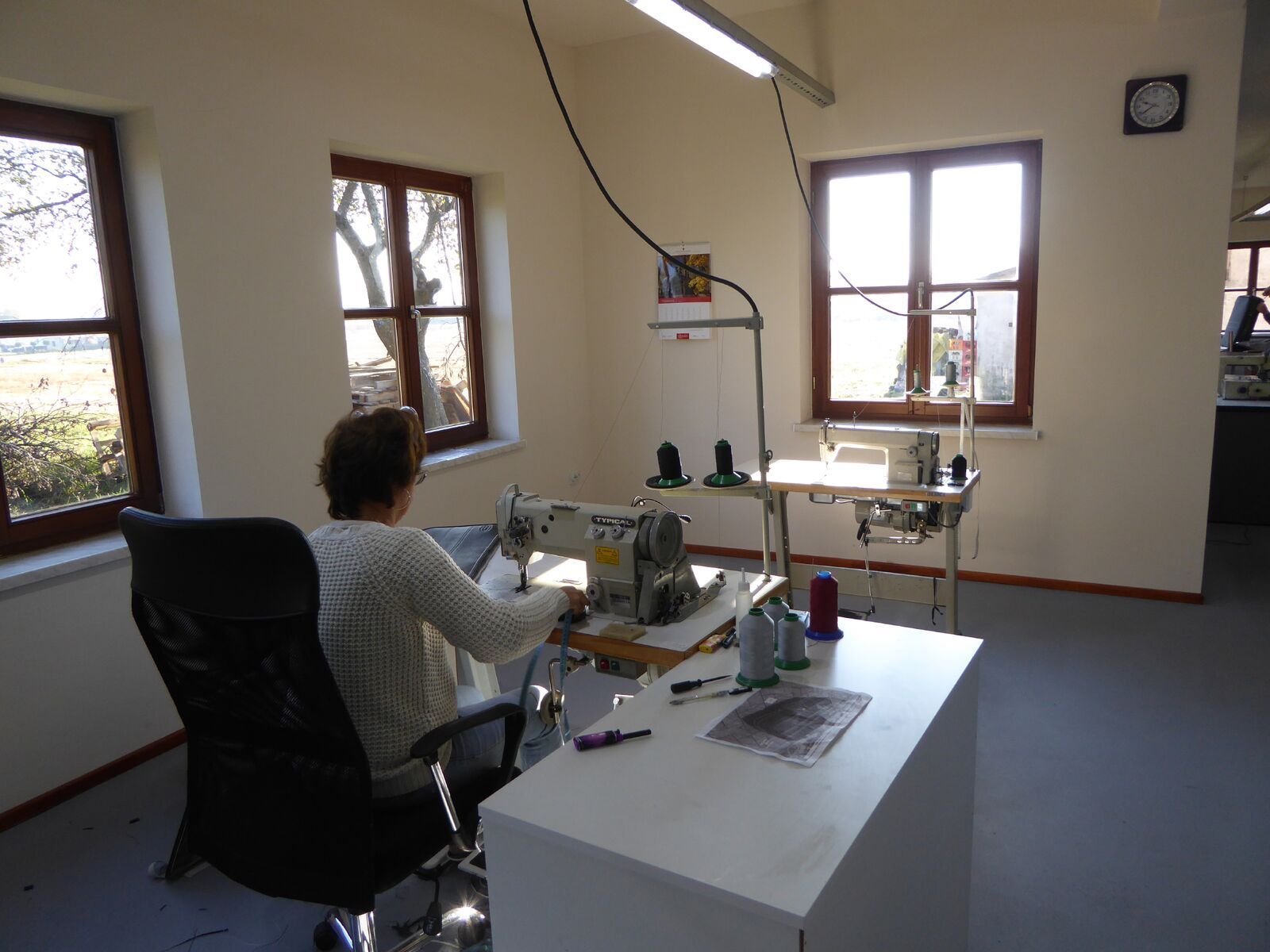 Een vrouw zit aan een bureau voor een naaimachine.