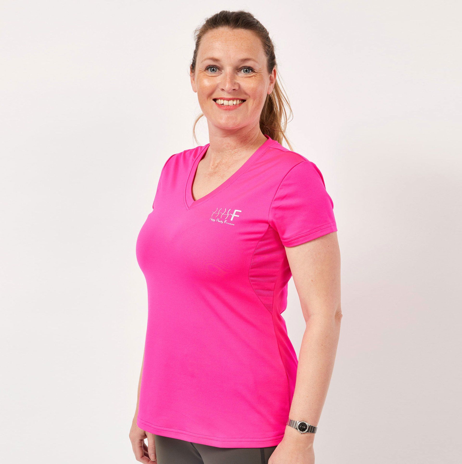 35+ lady wearing bright slimming design short sleeve athleisure top with Happy Healthy Fitness logo on it
