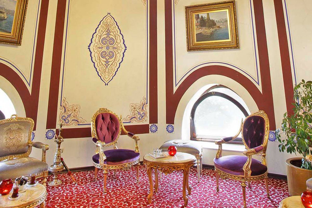 A living room with a red carpet , chairs , tables and paintings on the wall.