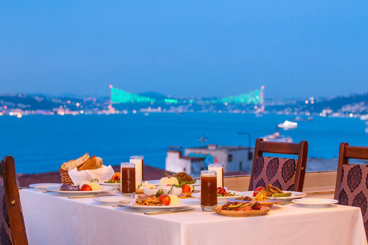 A table with plates of food and drinks on it with a view of the ocean.