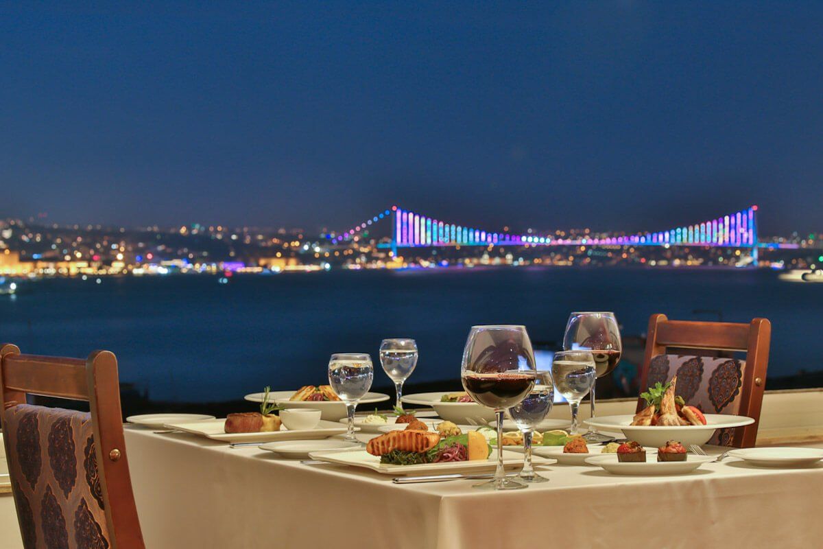 A table with plates of food and glasses of wine with a bridge in the background.