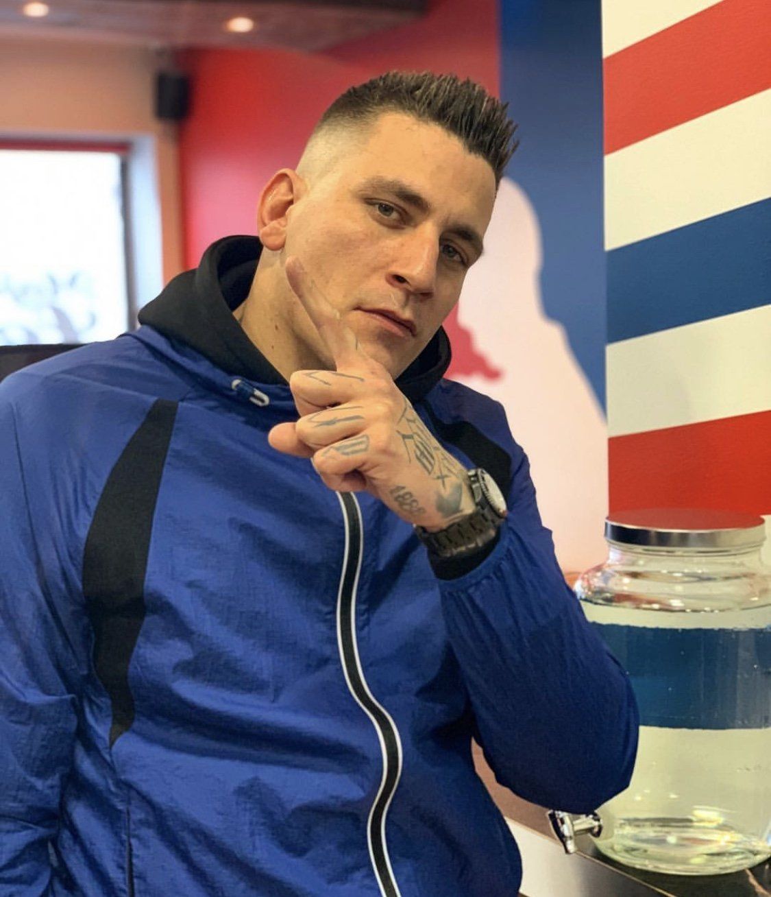 Ein Mann in einer blauen Jacke steht vor einer rot-weiß-blau gestreiften Wand