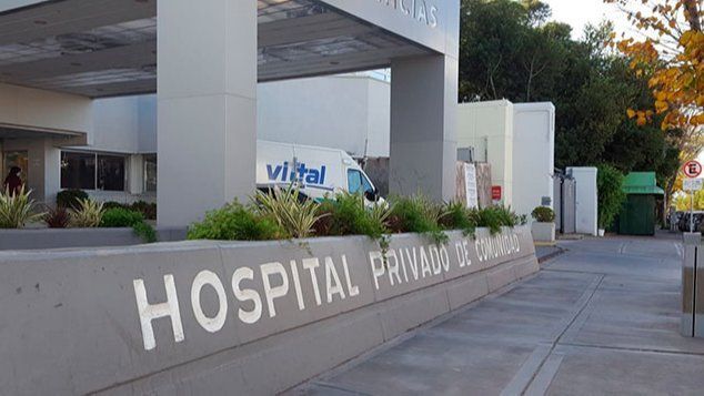 Letrero de entrada del hospital en un edificio moderno con acera y vegetación en el exterior.