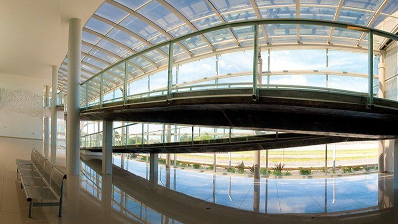 Piscina cubierta bajo un techo curvo de cristal, con reflejos brillantes y un banco a lo largo del lado izquierdo.