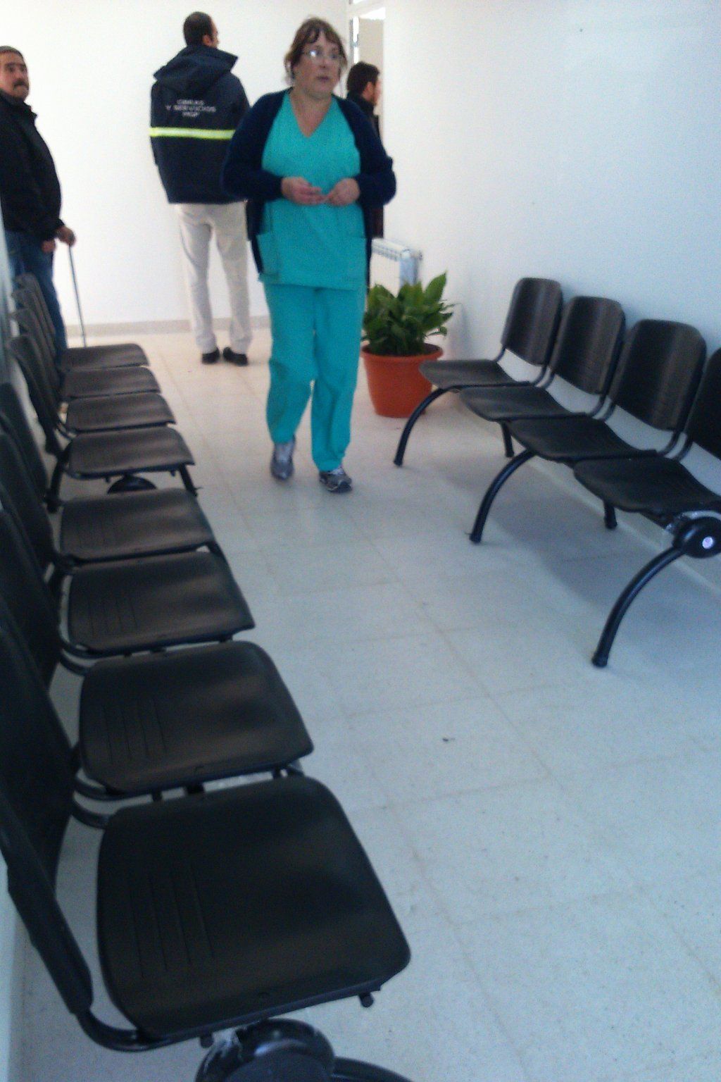 Dos personas en un pasillo con filas de sillas negras y una planta en maceta en el suelo.