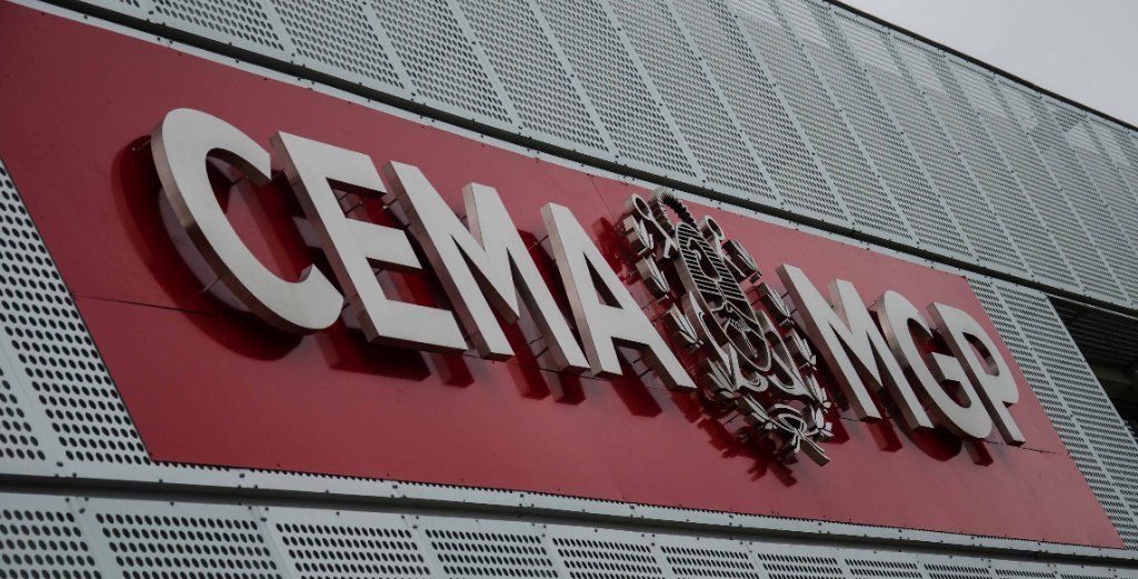 Logotipo de CEMA-MG en un letrero rojo montado en la fachada de un edificio gris.
