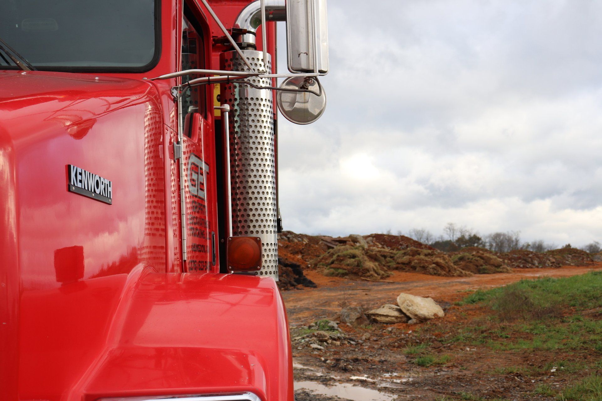 A red semi truck is parked in a dirt field.