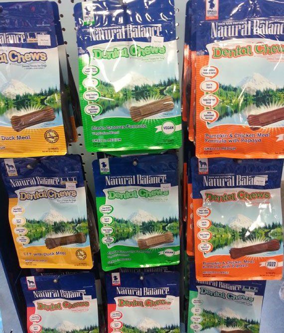 Colorful packs of Natural Harvest dental chews stacked on a shelf in blue, green, orange, and yellow packaging