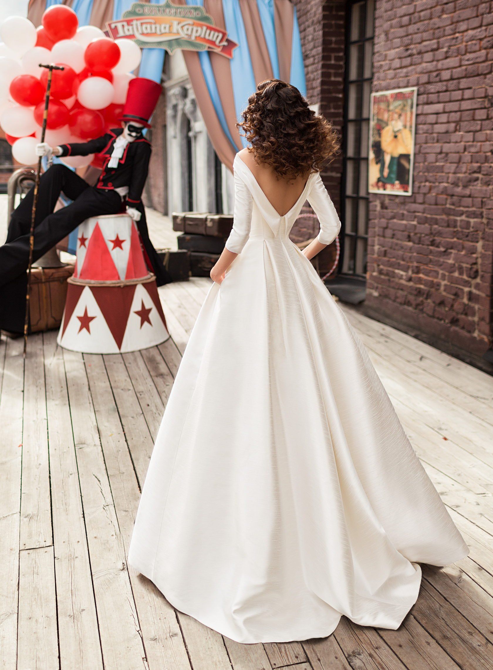 Eine Frau in einem weißen Brautkleid steht vor einem Zirkuszelt mit Luftballons.