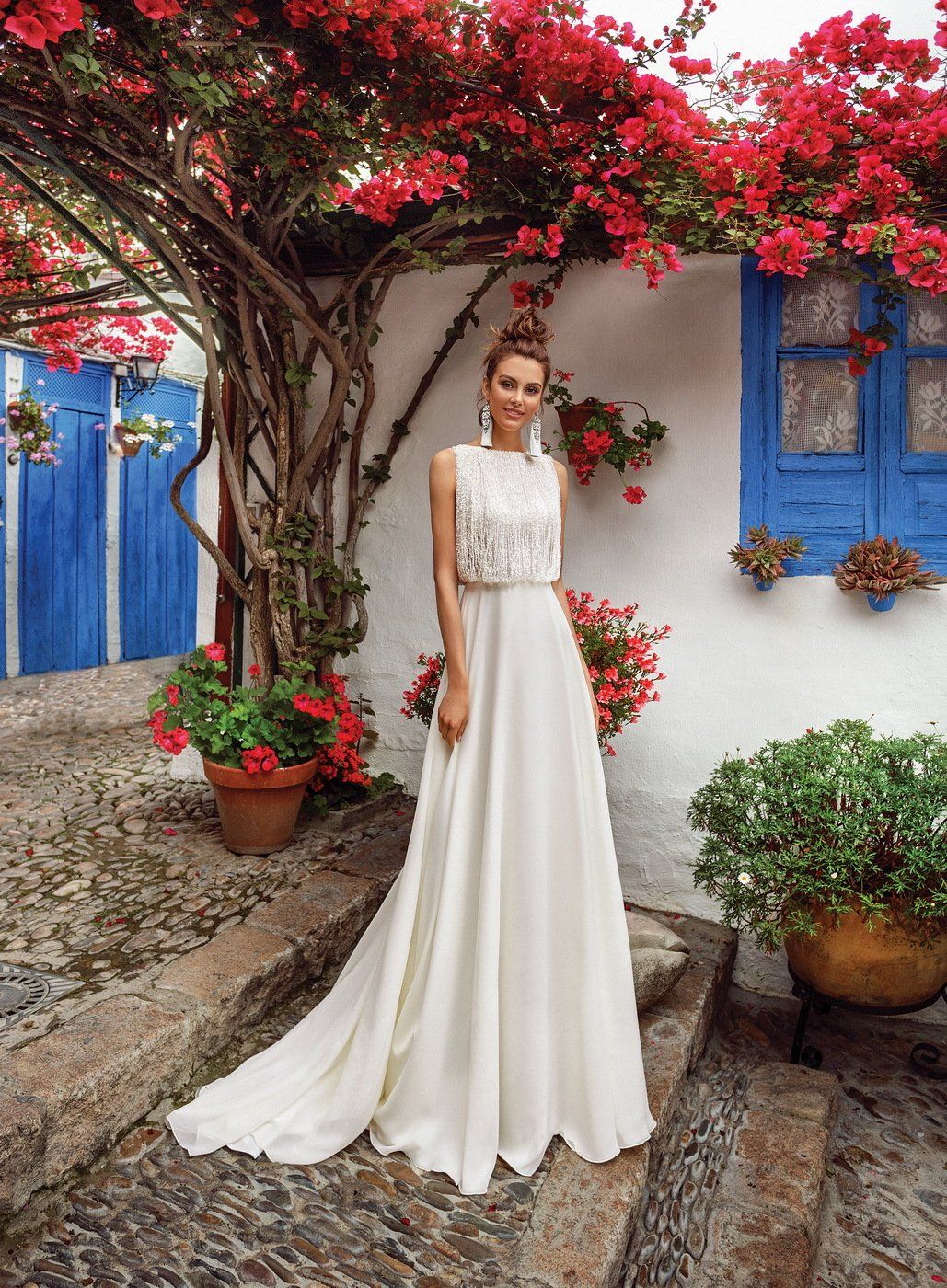 Eine Frau in einem weißen Kleid steht unter einem Baum mit roten Blüten.