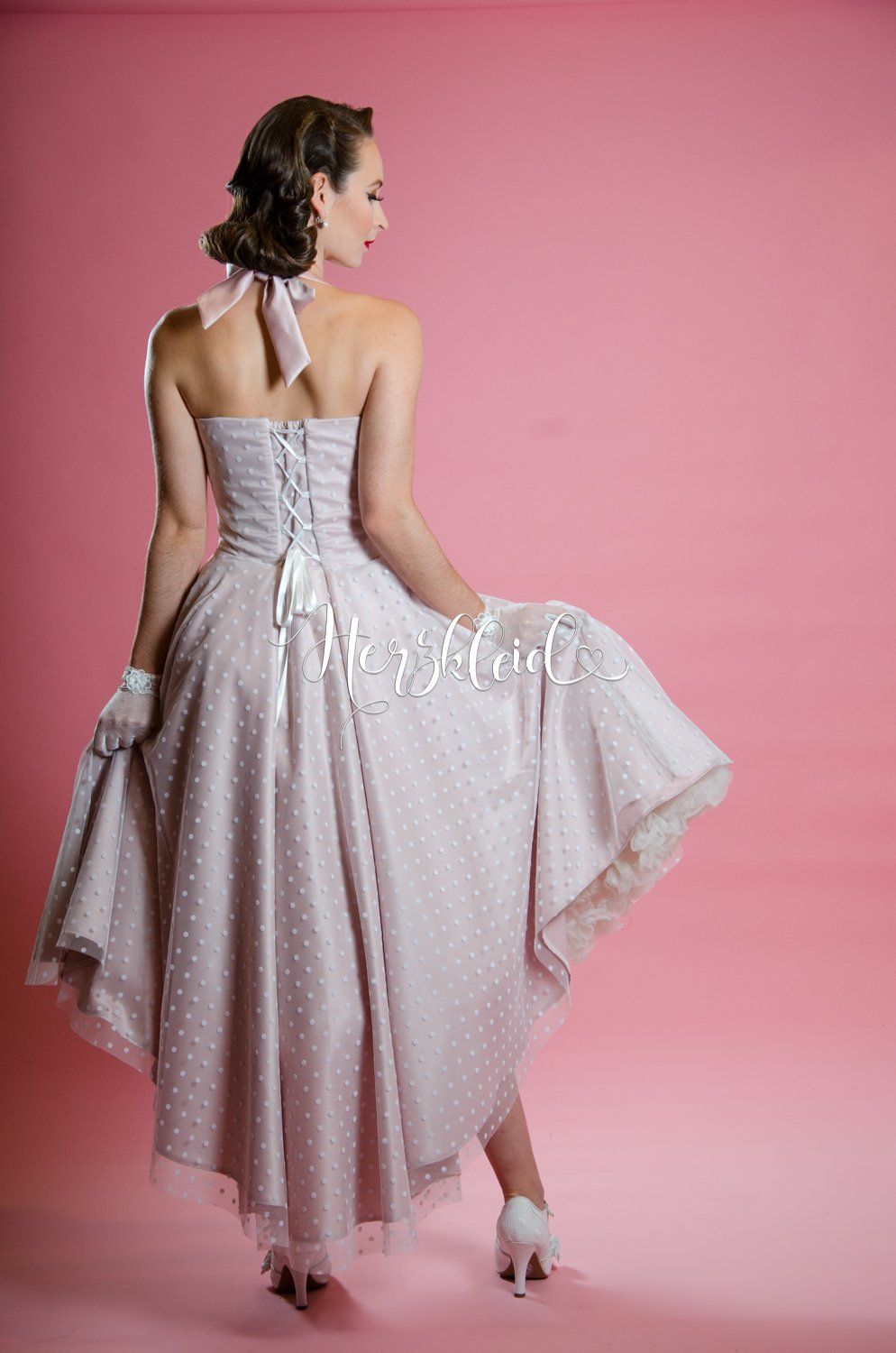 Der Rücken einer Frau in einem gepunkteten Kleid auf rosa Hintergrund.