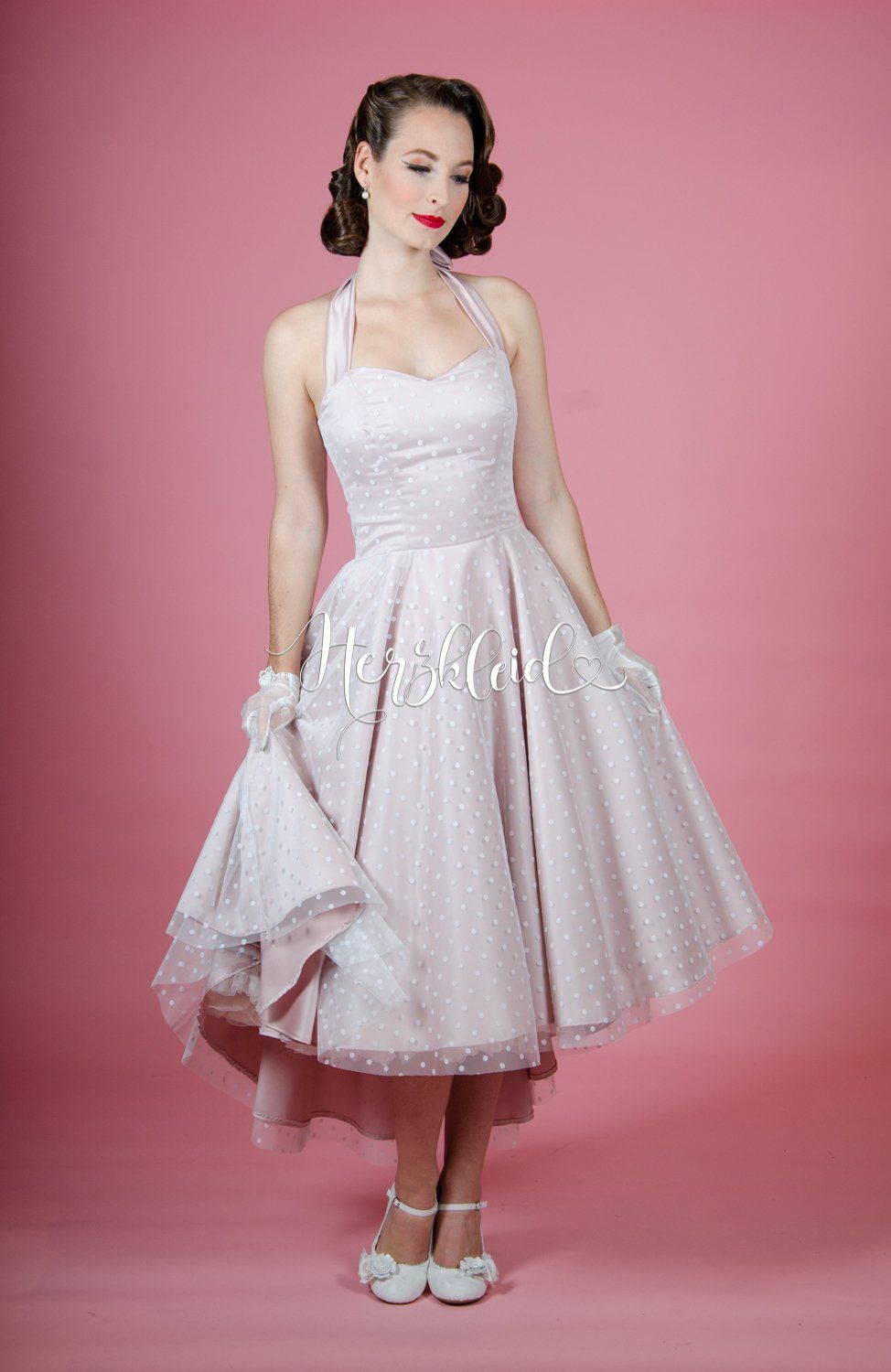 Eine Frau in einem weißen Kleid steht vor einem rosa Hintergrund.