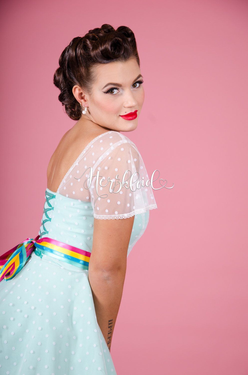 Eine Frau in einem blauen Kleid steht vor einem rosa Hintergrund.