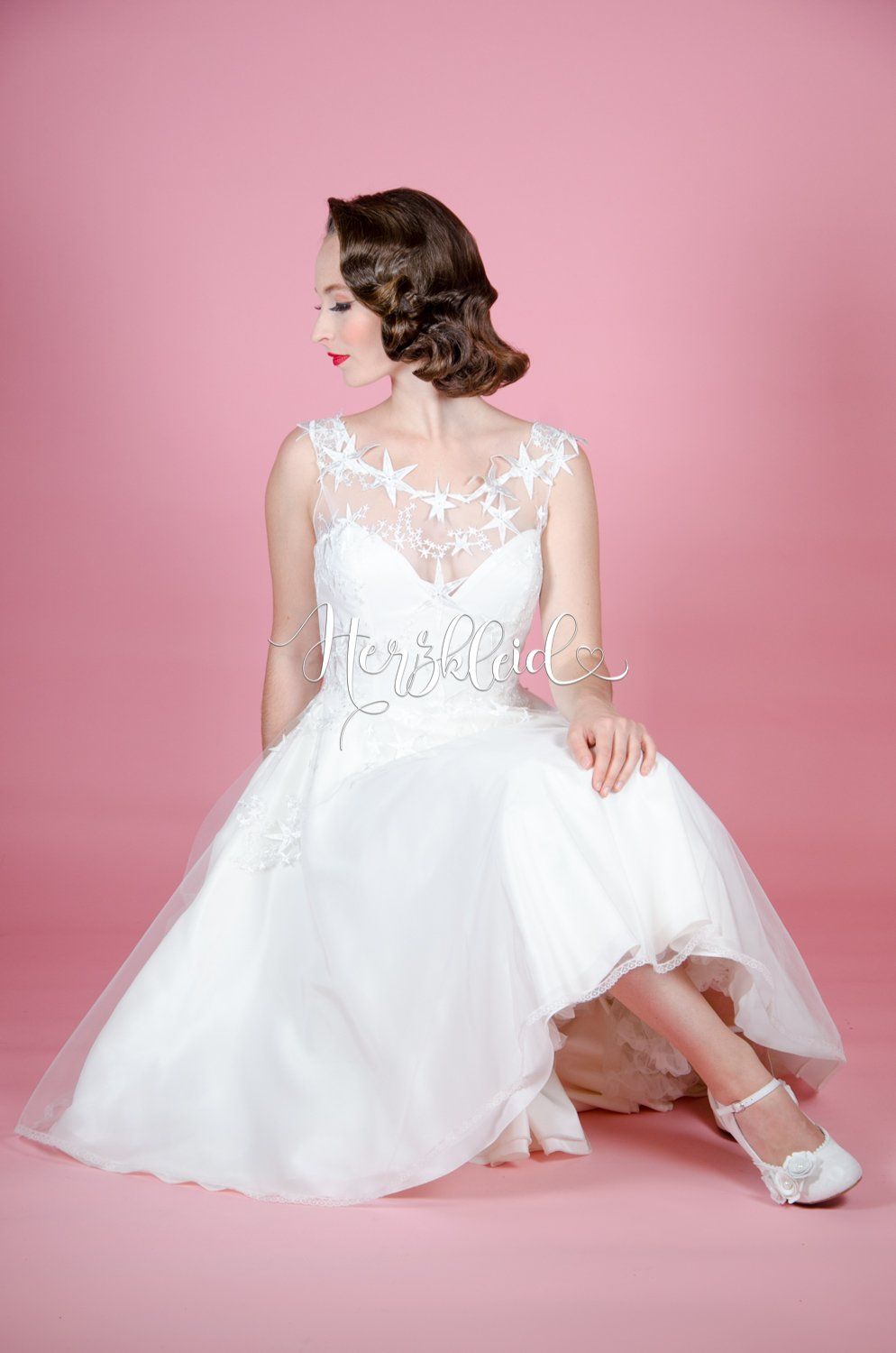 Eine Frau in einem weißen Brautkleid sitzt vor einem rosa Hintergrund auf dem Boden.