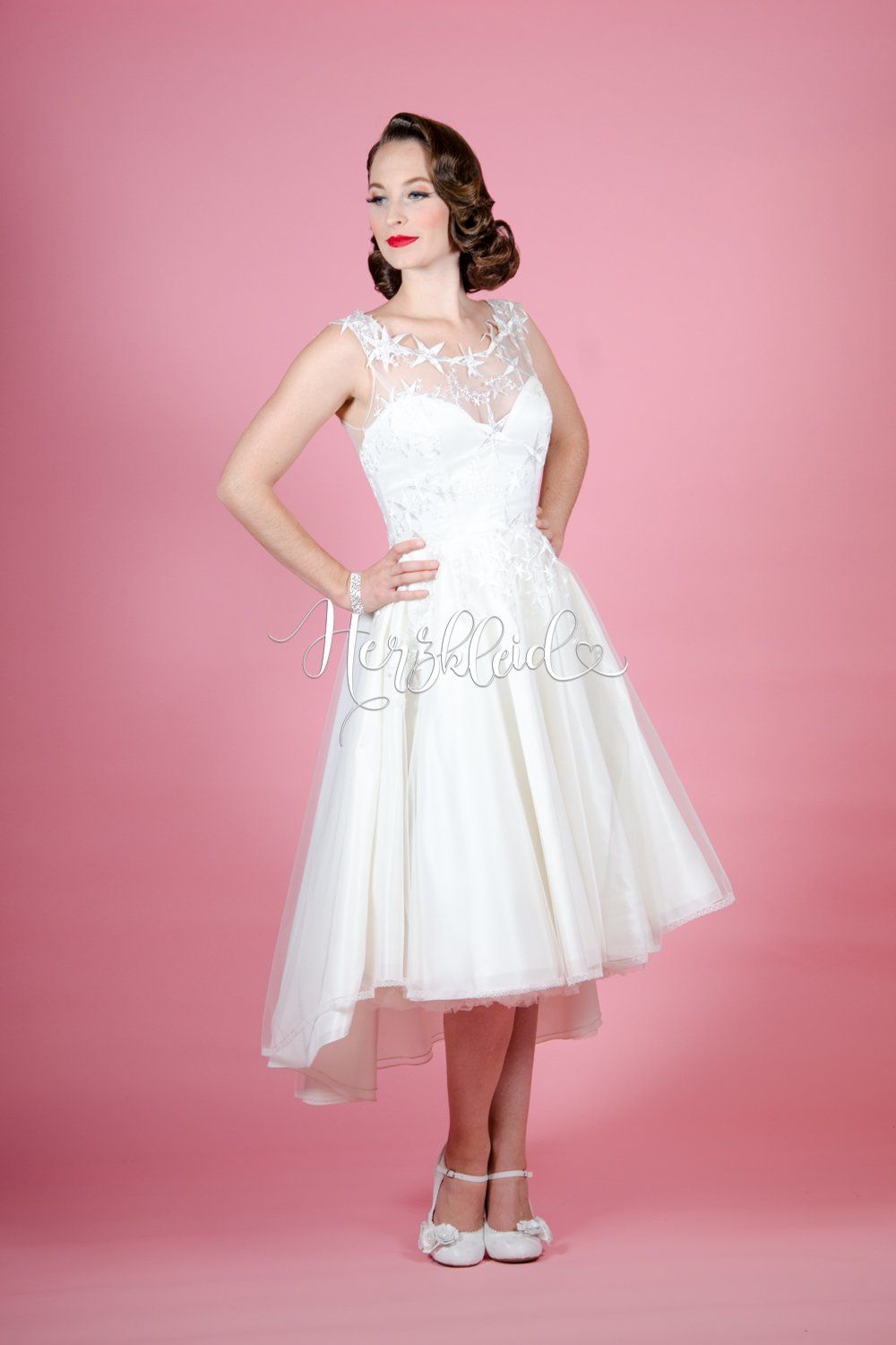 Eine Frau in einem weißen Kleid steht vor einem rosa Hintergrund.