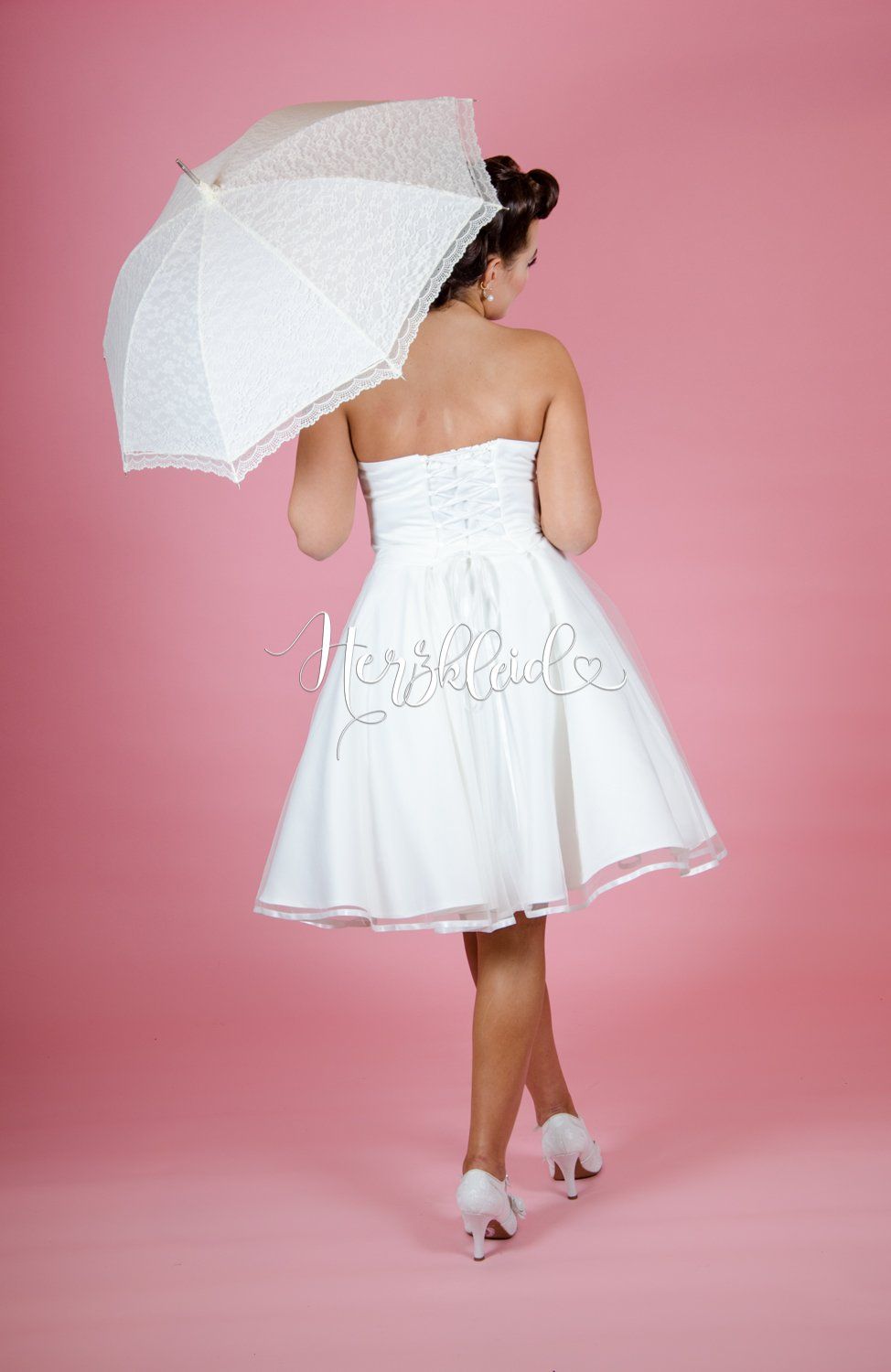 Eine Frau in einem weißen Kleid hält einen Regenschirm.