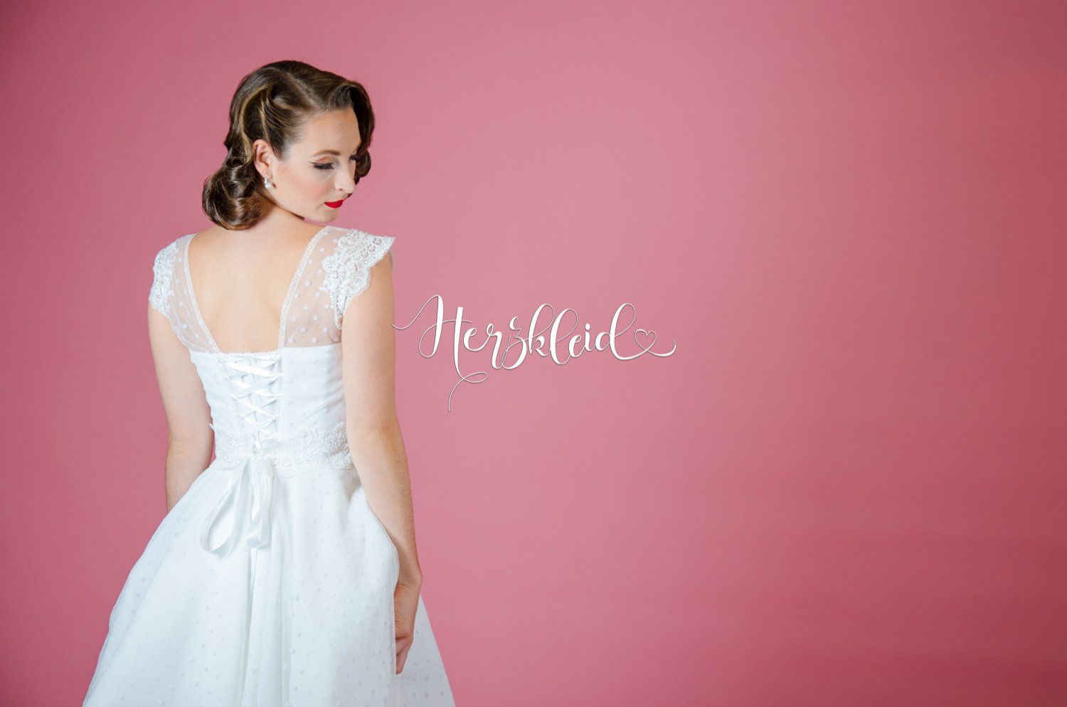 Eine Frau in einem weißen Brautkleid steht vor einem rosa Hintergrund.