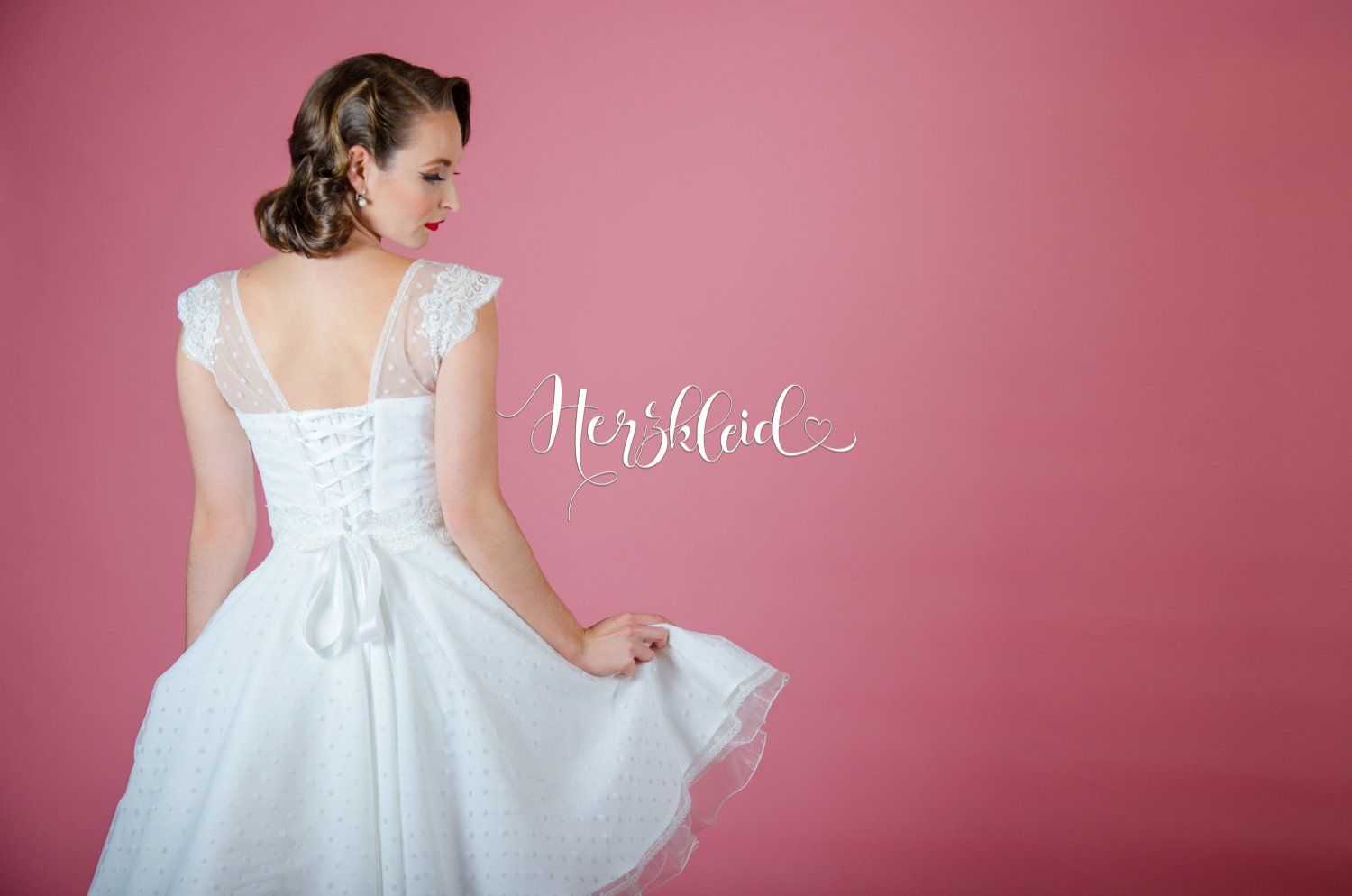 Eine Frau in einem weißen Kleid steht vor einem rosa Hintergrund.