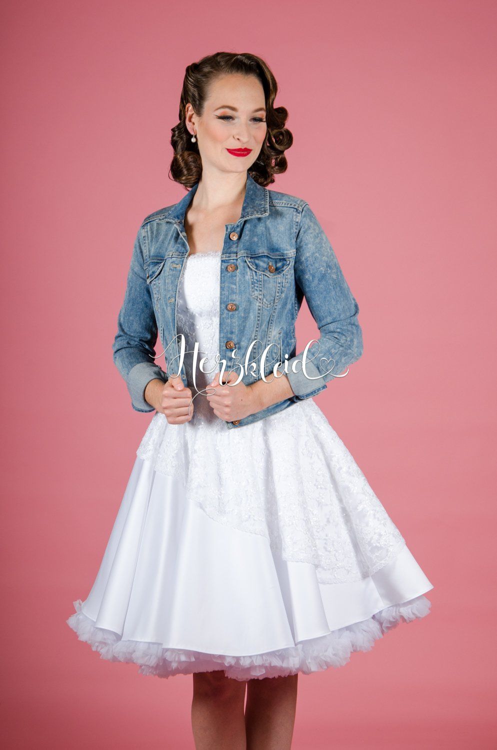 Eine Frau trägt ein weißes Kleid und eine Jeansjacke.
