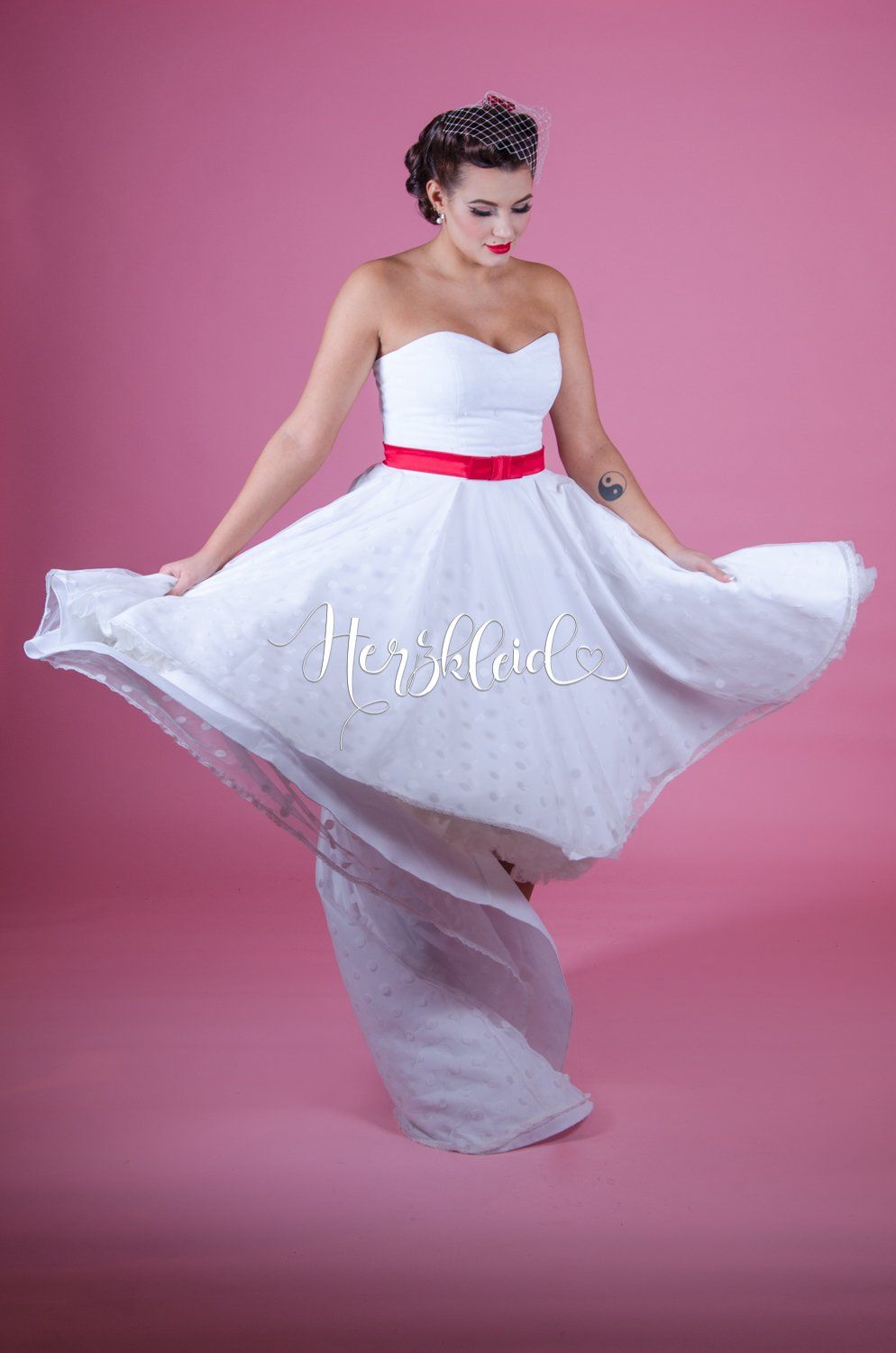 Eine Frau trägt ein weißes Brautkleid mit einer roten Schärpe.
