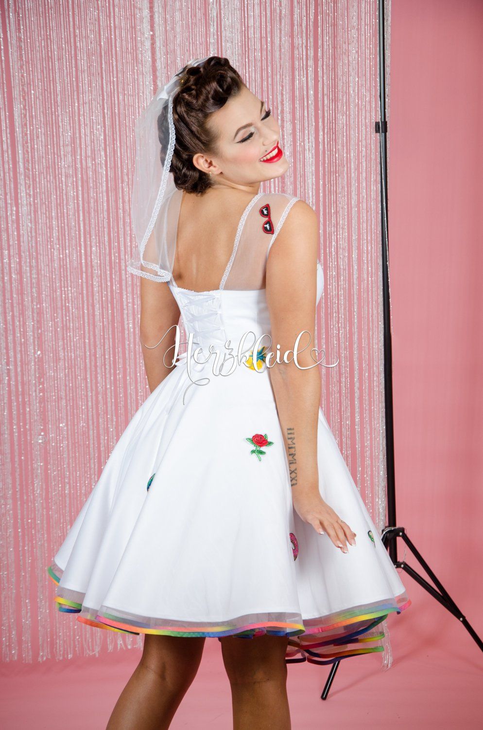 Eine Frau in einem weißen Kleid und Schleier steht vor einem rosa Vorhang.