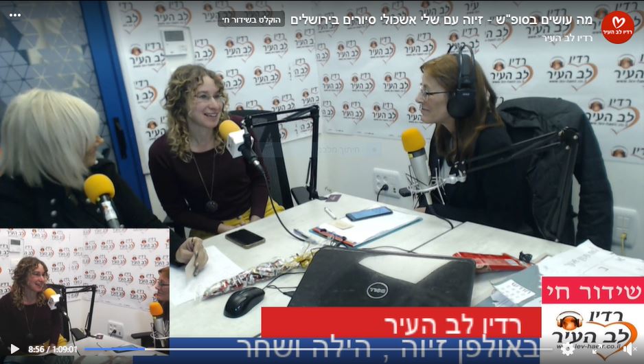Three women in a radio studio at a table with microphones, a laptop, and headphones. Smiling, talking.