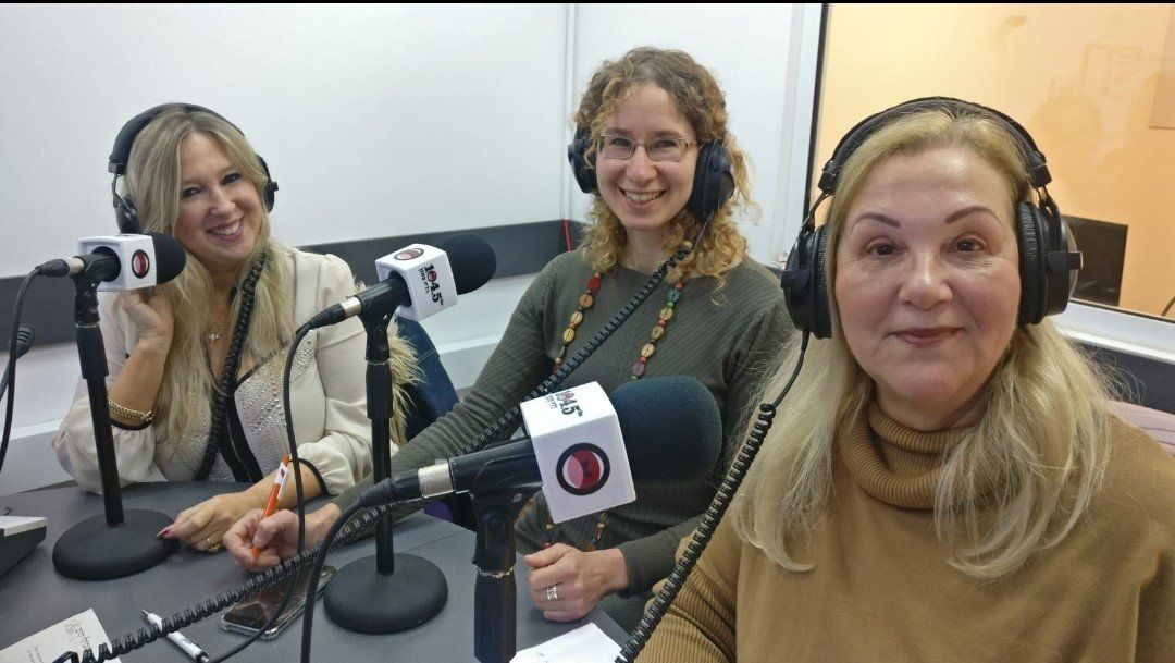 Three women wearing headphones and speaking into microphones in a radio studio setting.