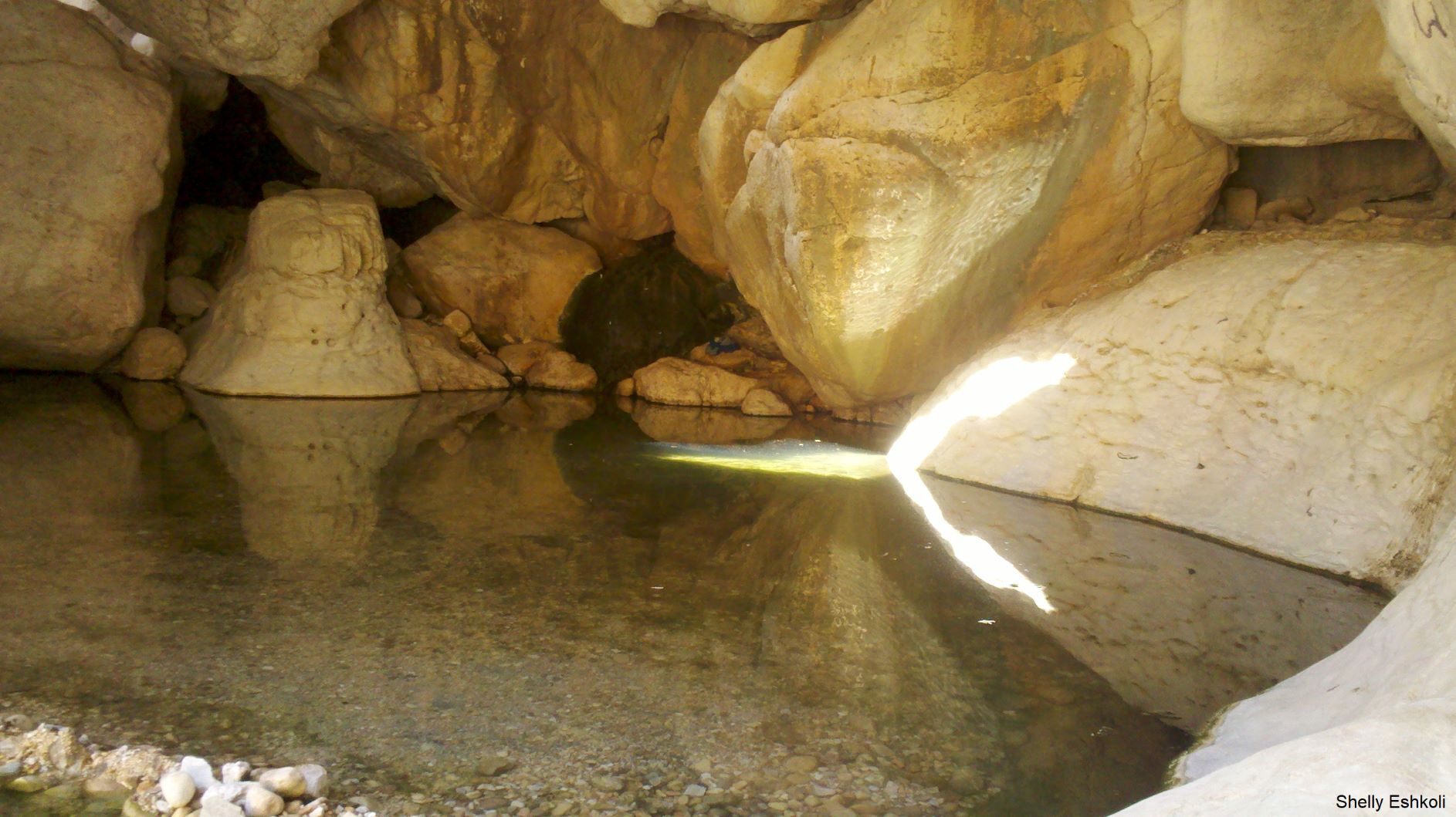 Cave interior with a still pool of water reflecting the light and surrounding rock formations.