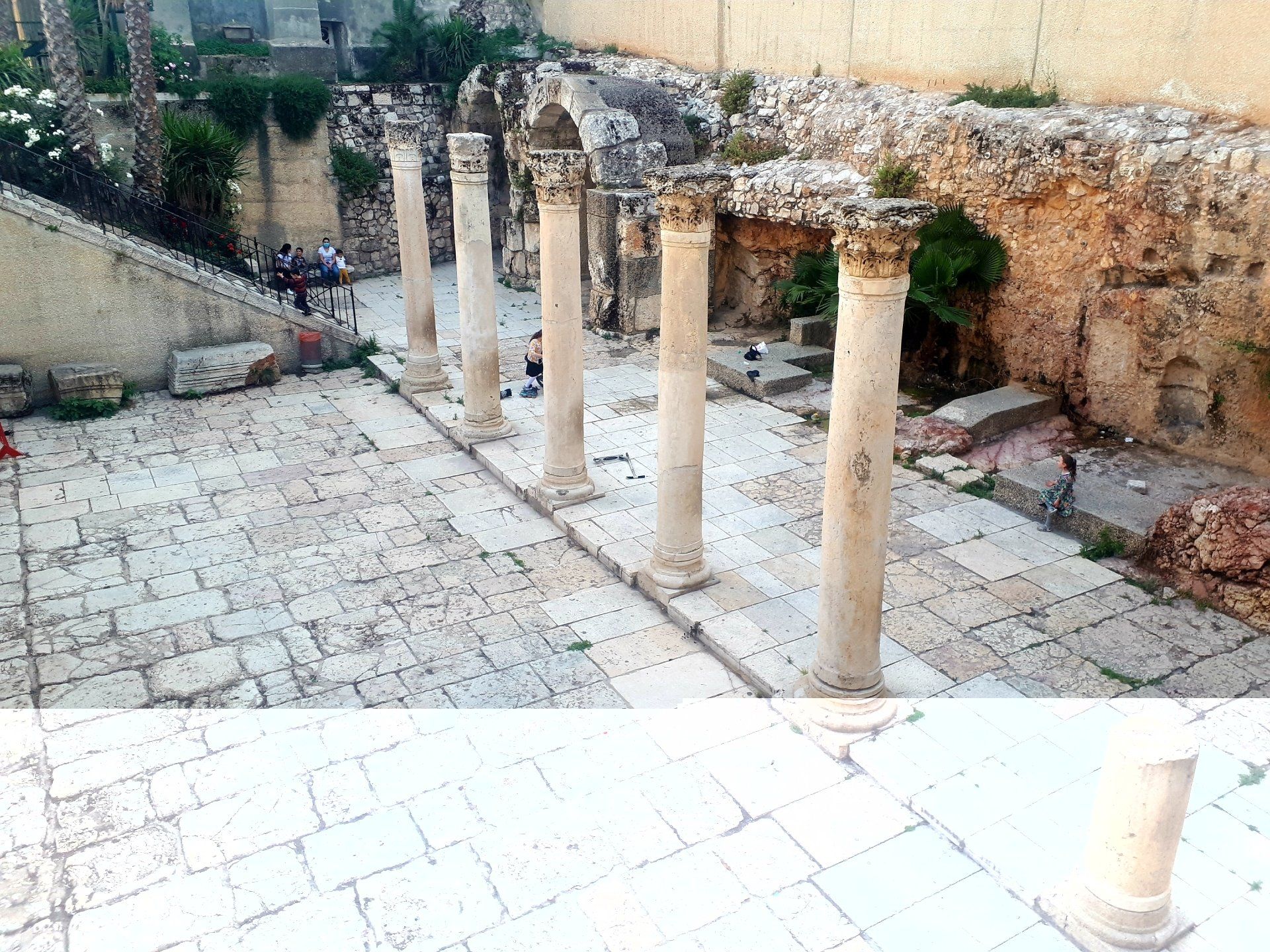 Columns line a stone walkway, likely in an ancient ruin. Sunlight highlights the columns and surrounding stone.