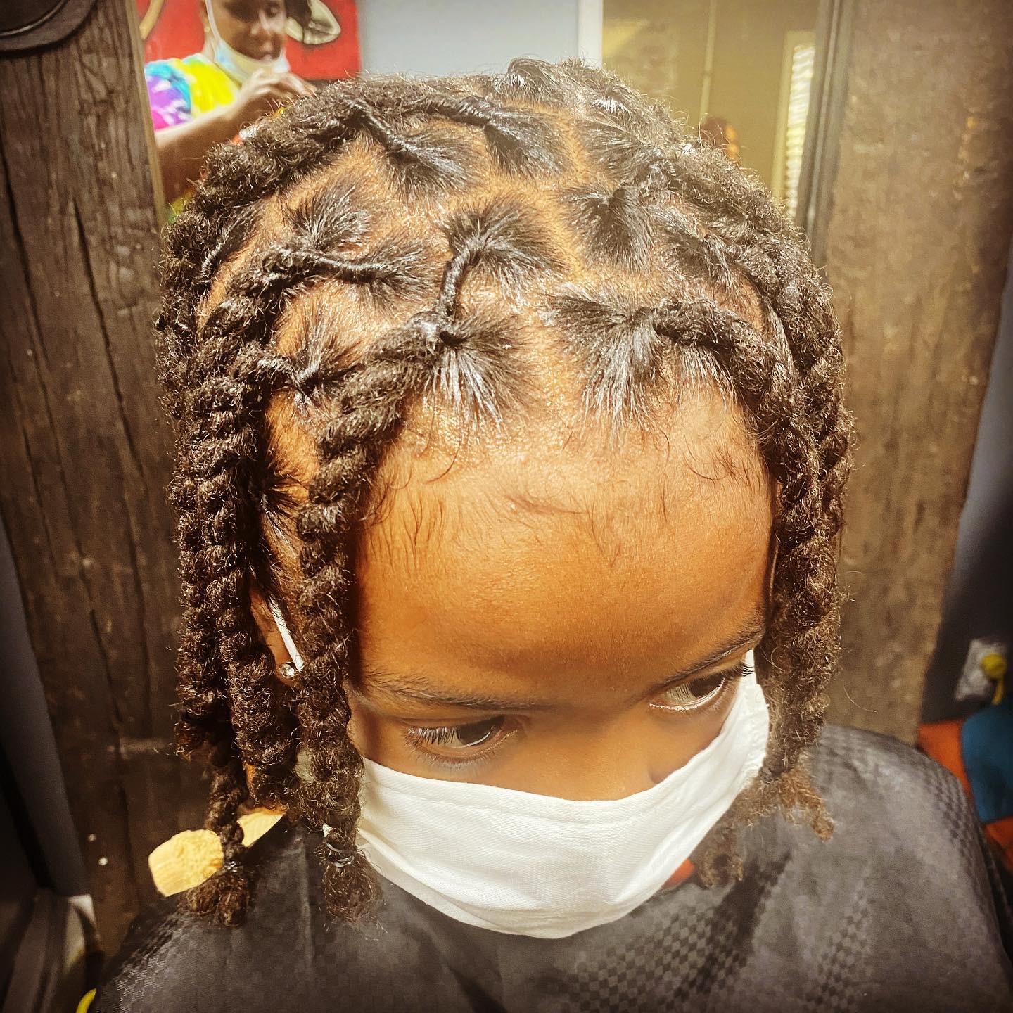 A young boy with dreadlocks is wearing a face mask.