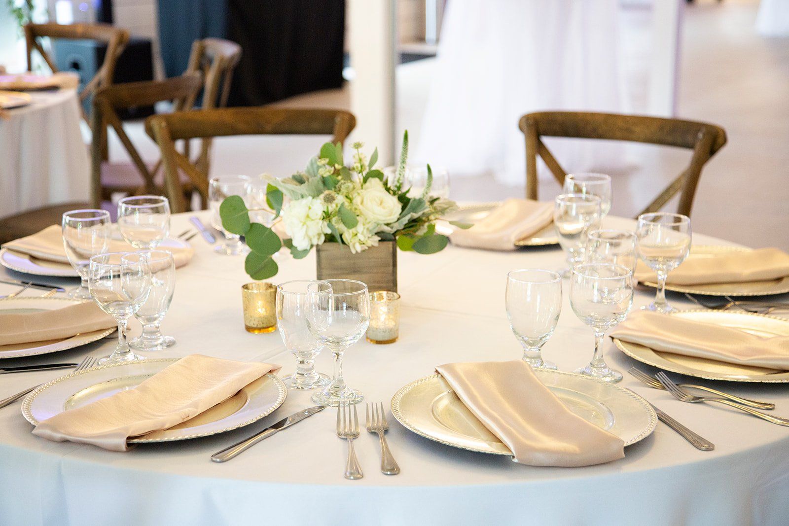 Elegant banquet table set with white plates, gold napkins, glassware, and a floral centerpiece on a white tablecloth