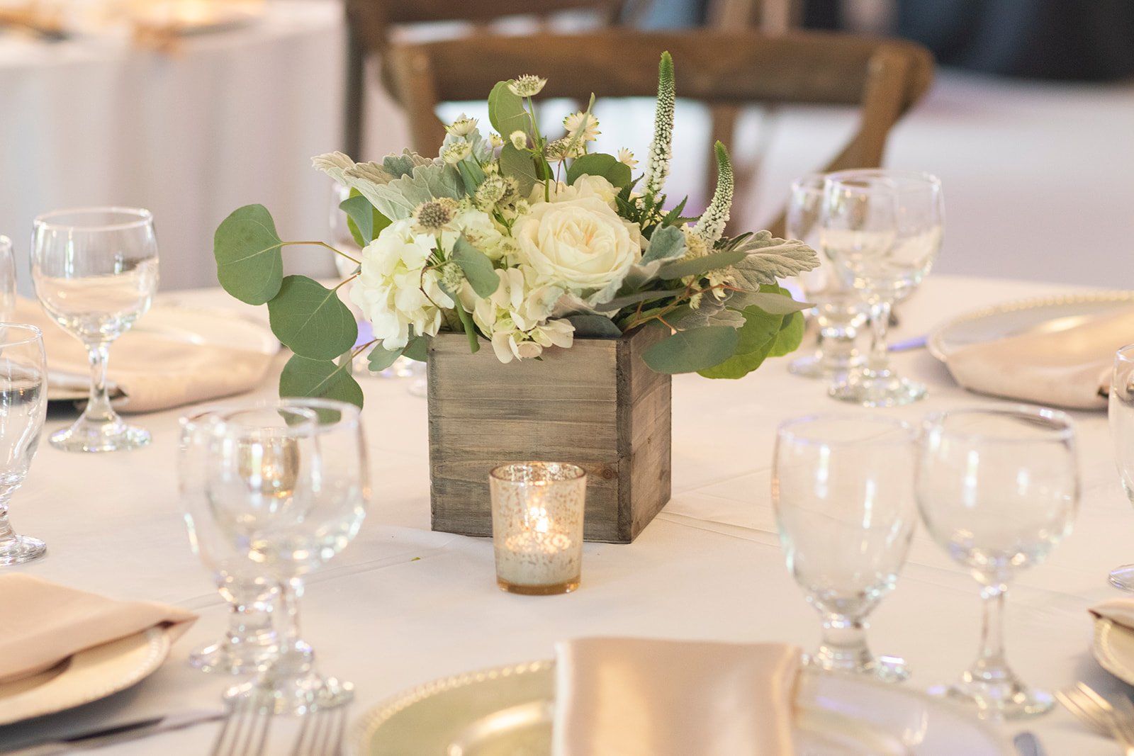 Elegant wedding reception table with white floral centerpiece, candles, and glassware on a cream tablecloth