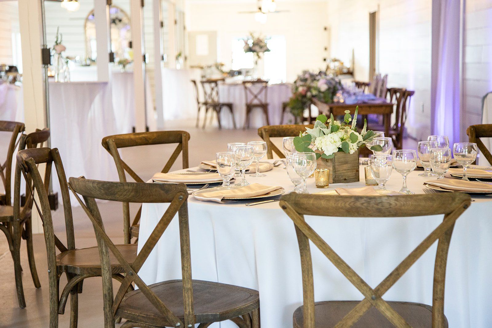 Elegant banquet hall with round, set tables and wooden chairs, decorated with white linens and floral centerpieces