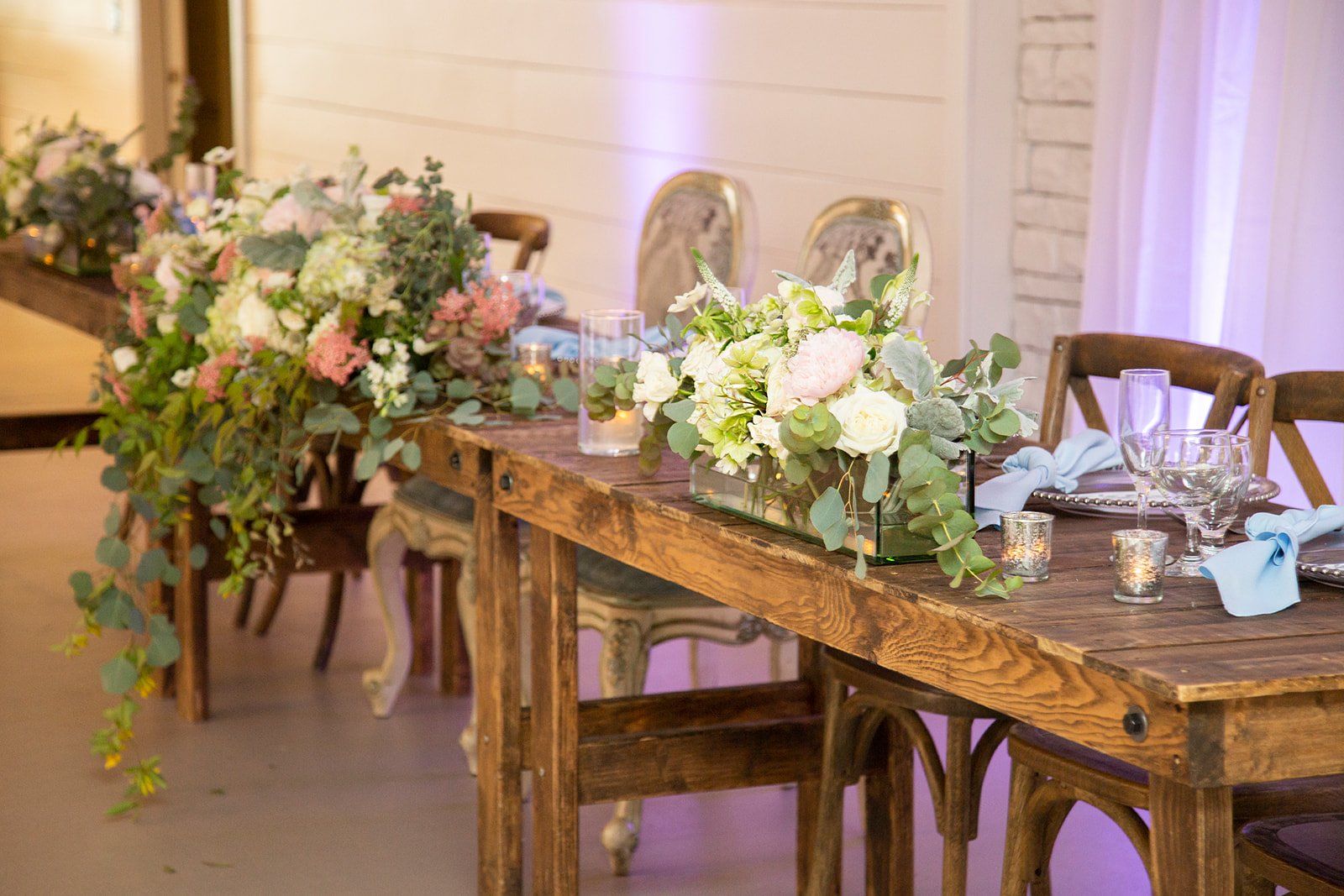 Floral arrangements on a rustic wooden table in a softly lit event venue