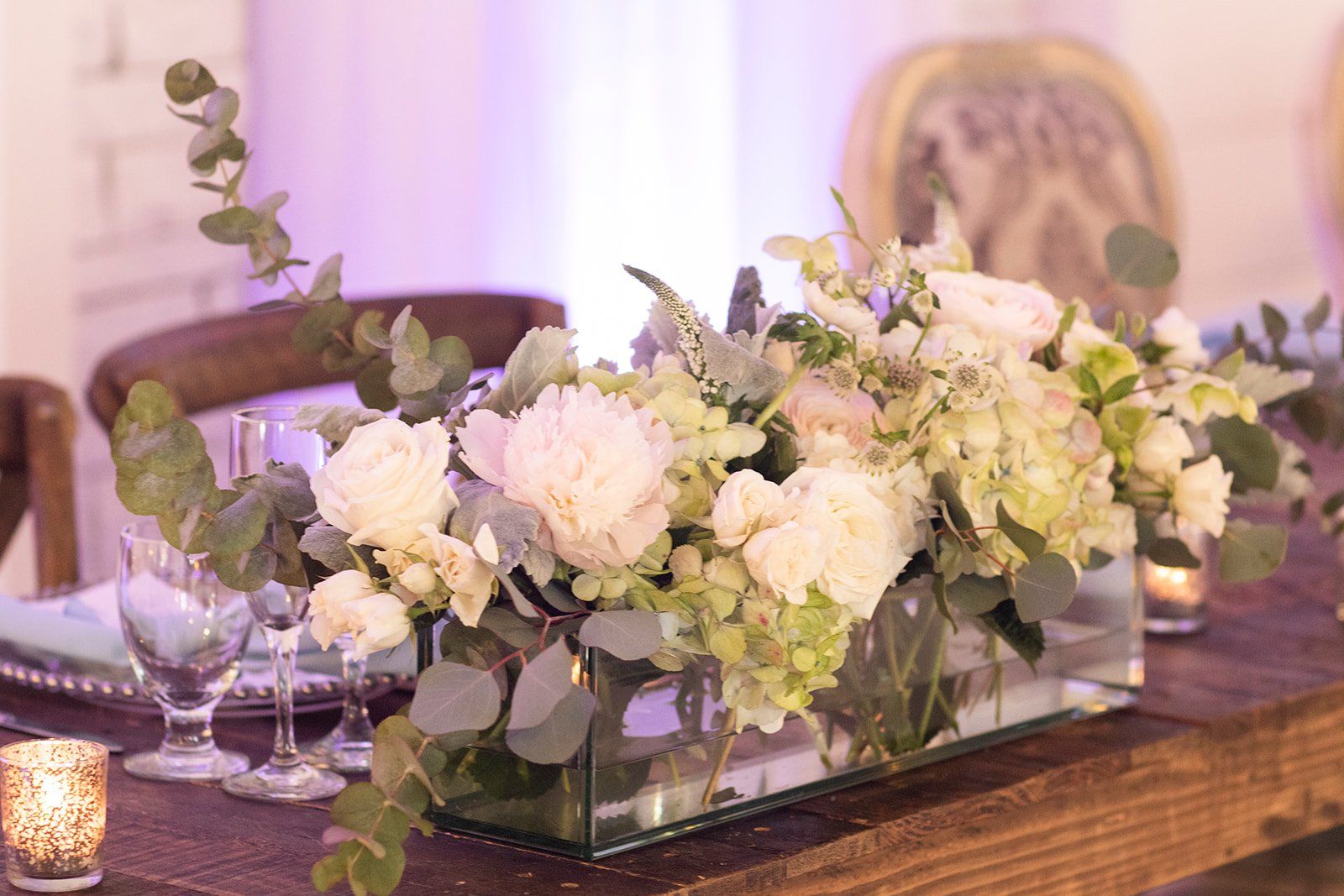 Elegant white and green floral centerpiece on a wooden table with candles and glassware