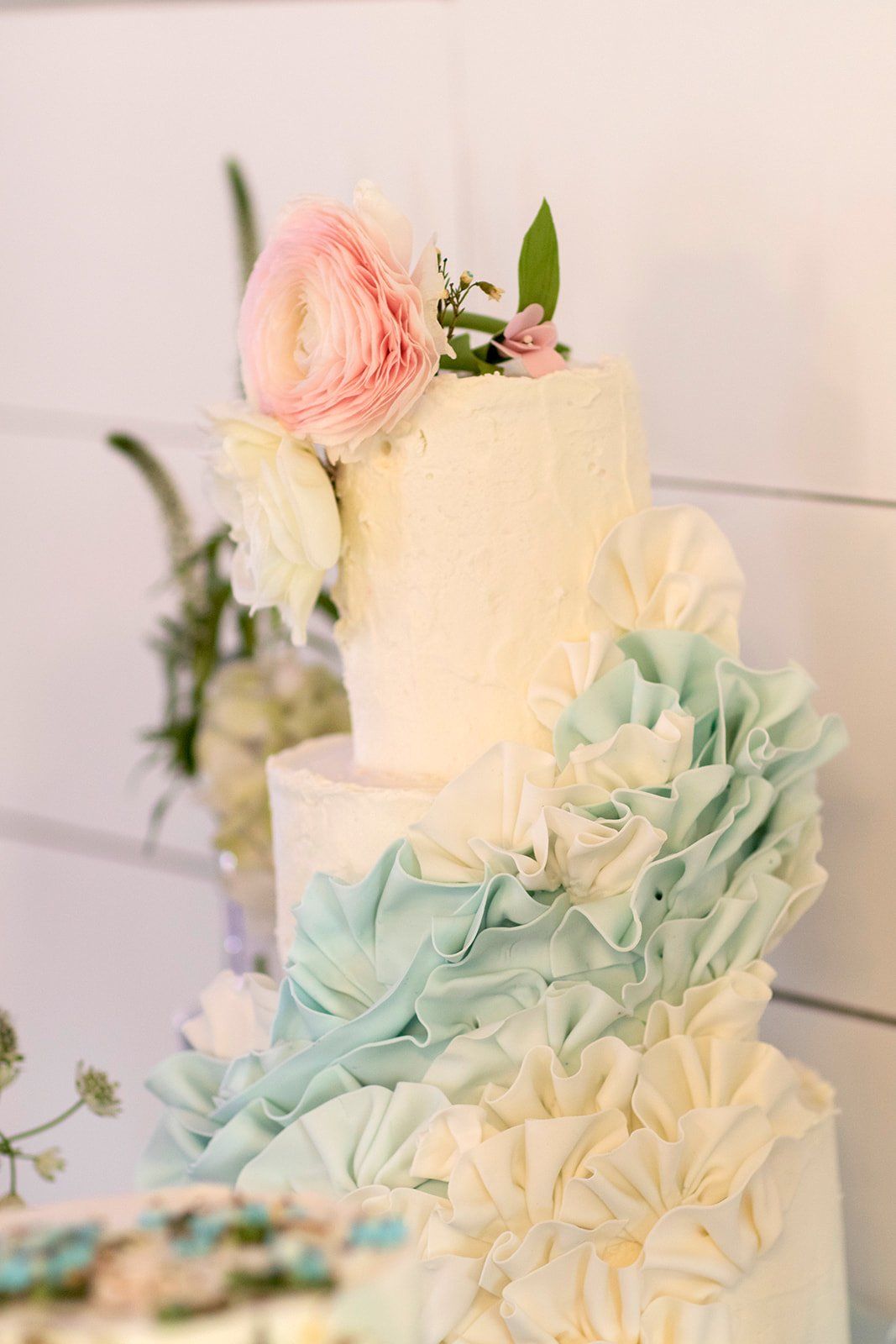 Three-tiered pastel floral cake with white and mint icing and pink flower accents