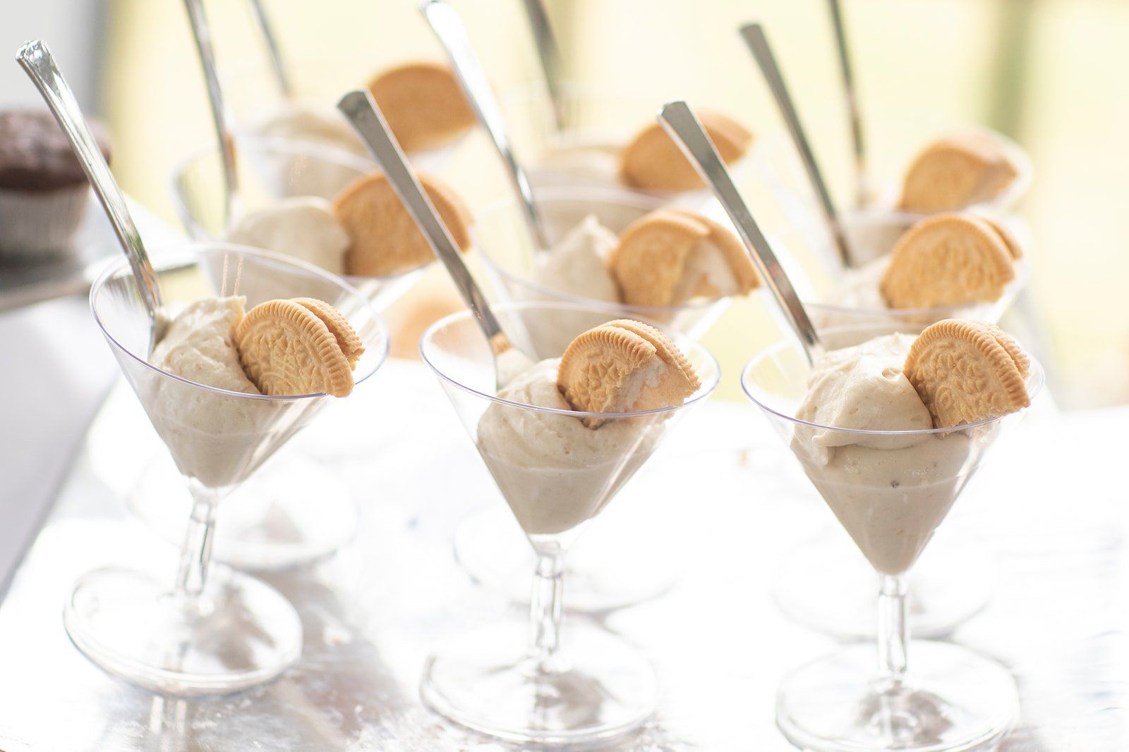 Martini glasses filled with creamy dessert, topped with cookies and spoons on a bright table