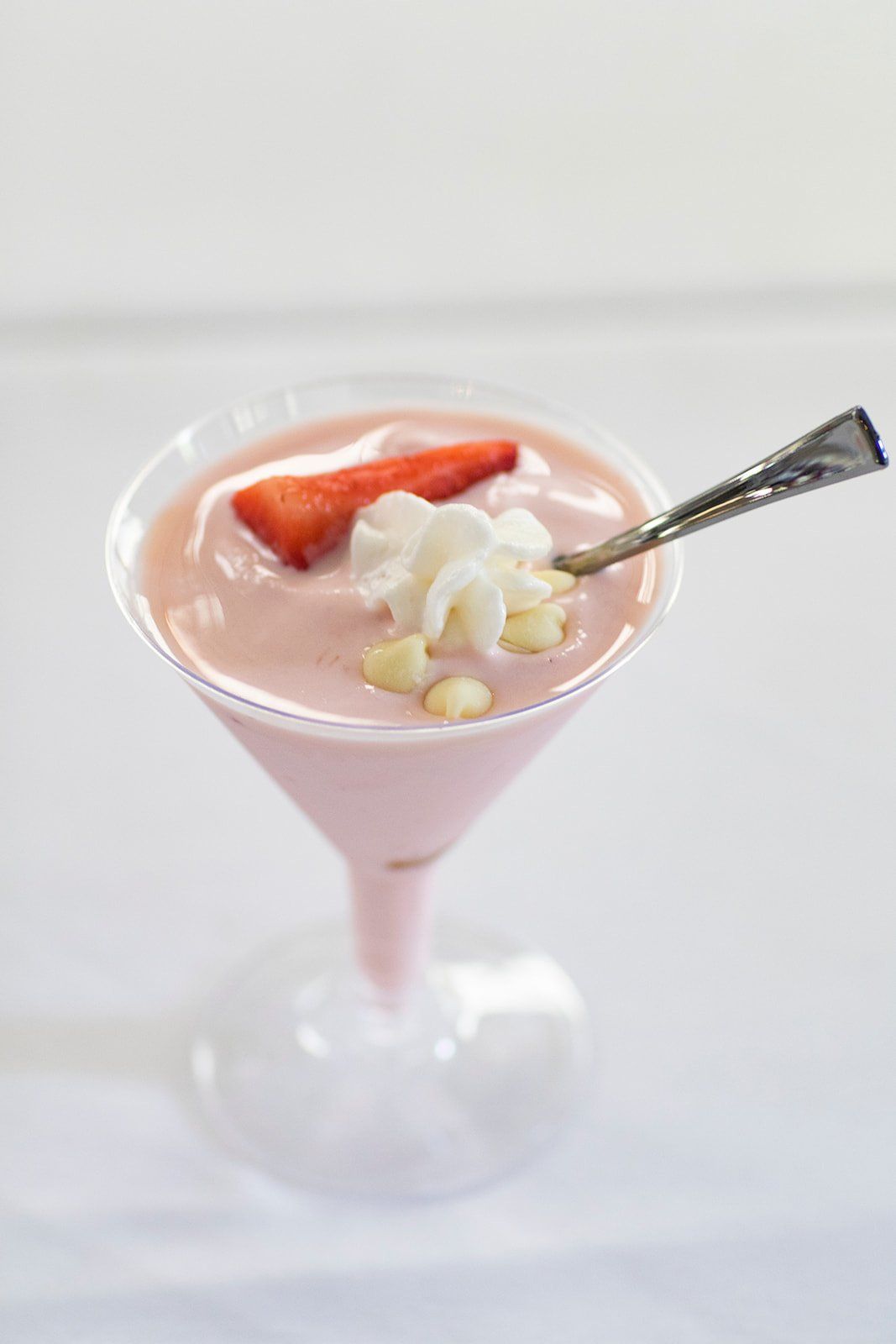 Pink strawberry milkshake in a glass, topped with whipped cream and a strawberry, with a spoon