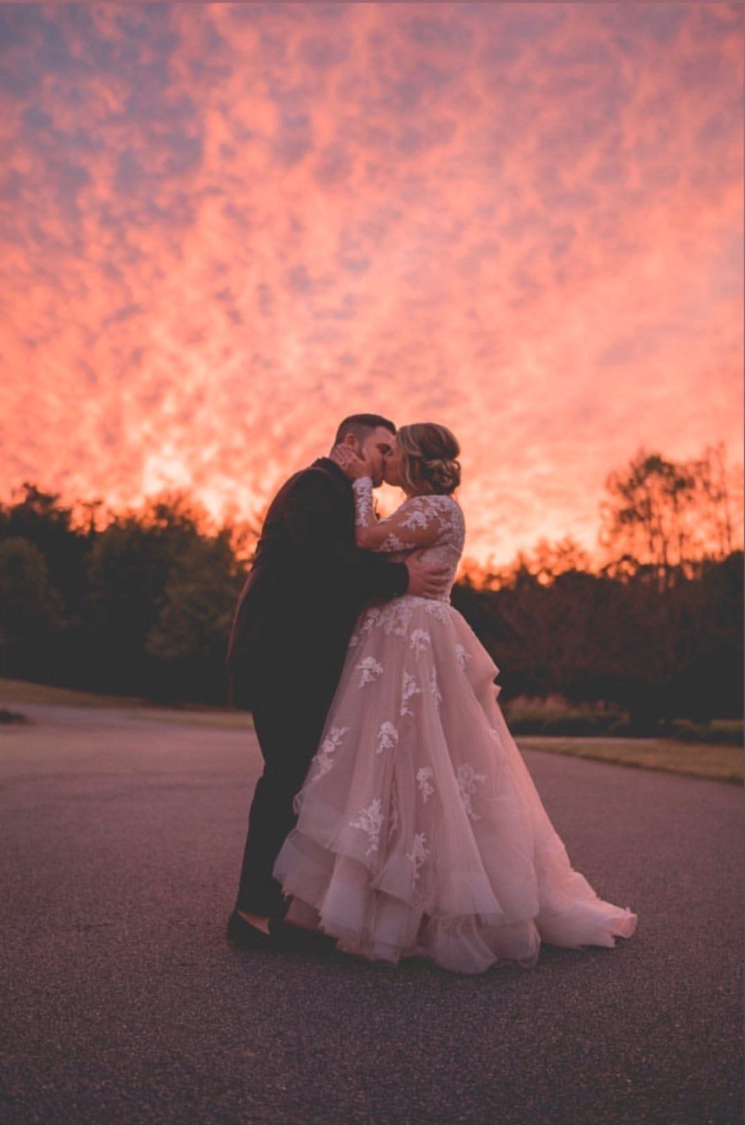 A bride and groom are kissing in front of a sunset.