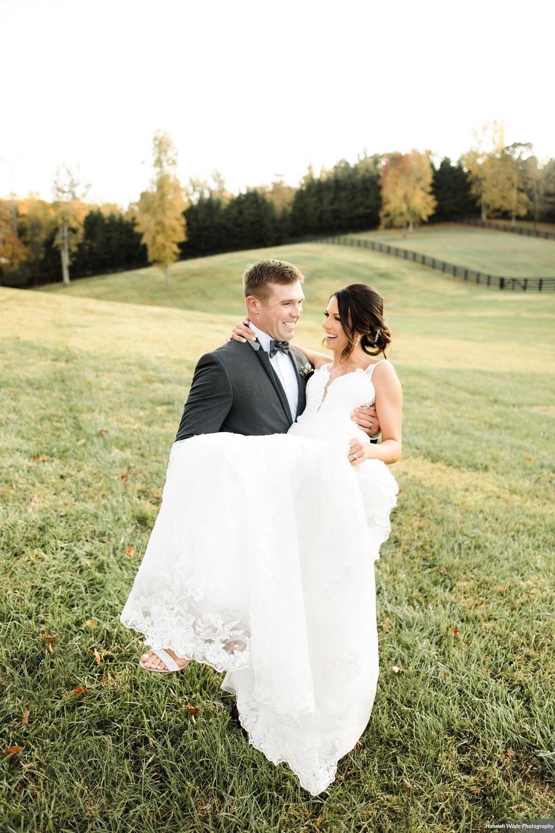 A groom is carrying his bride in his arms in a field.
