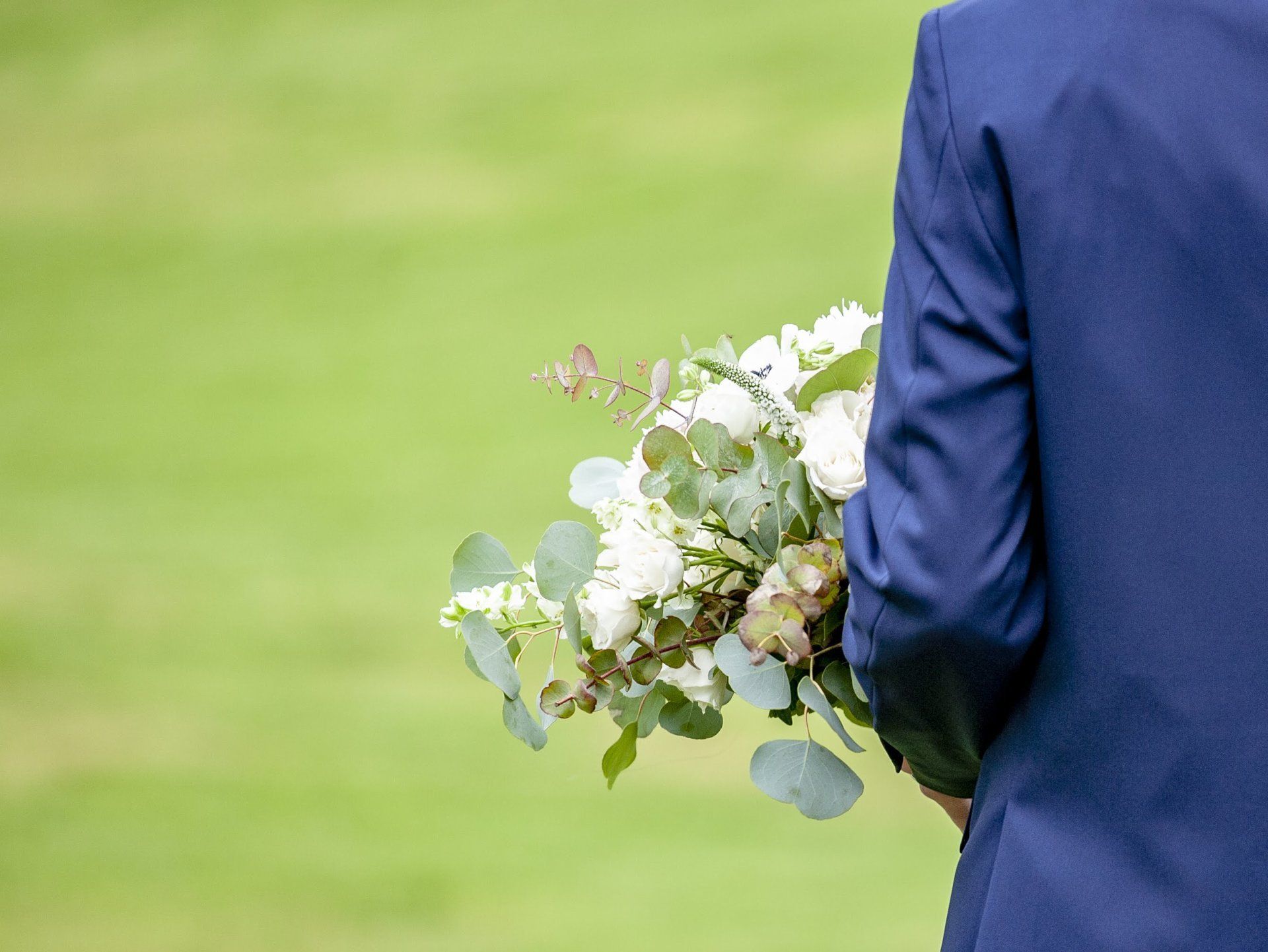 Person in a blue suit holding a bouquet of white flowers outdoors on a grassy field