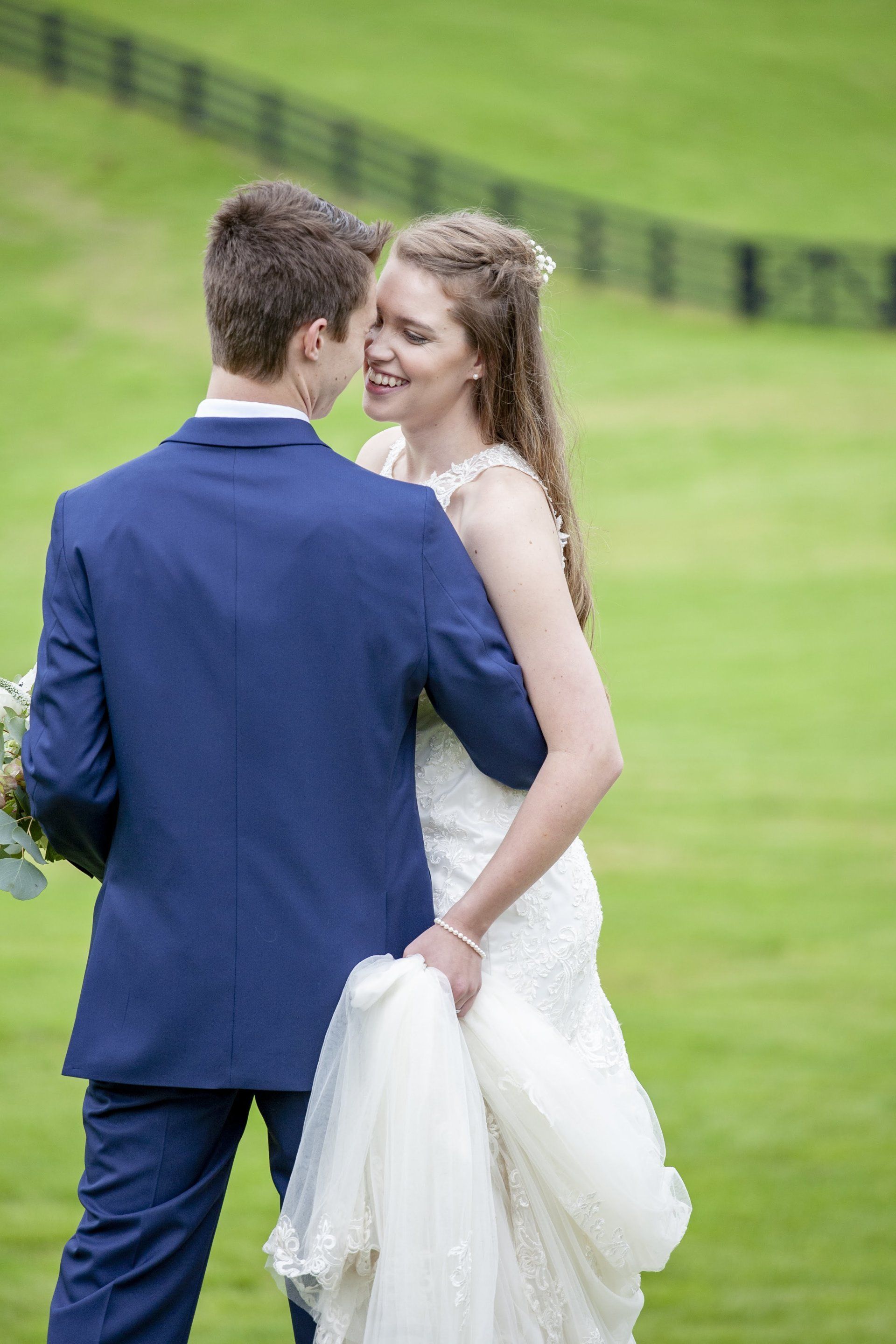 Bride and groom in formalwear embracing on a grassy field