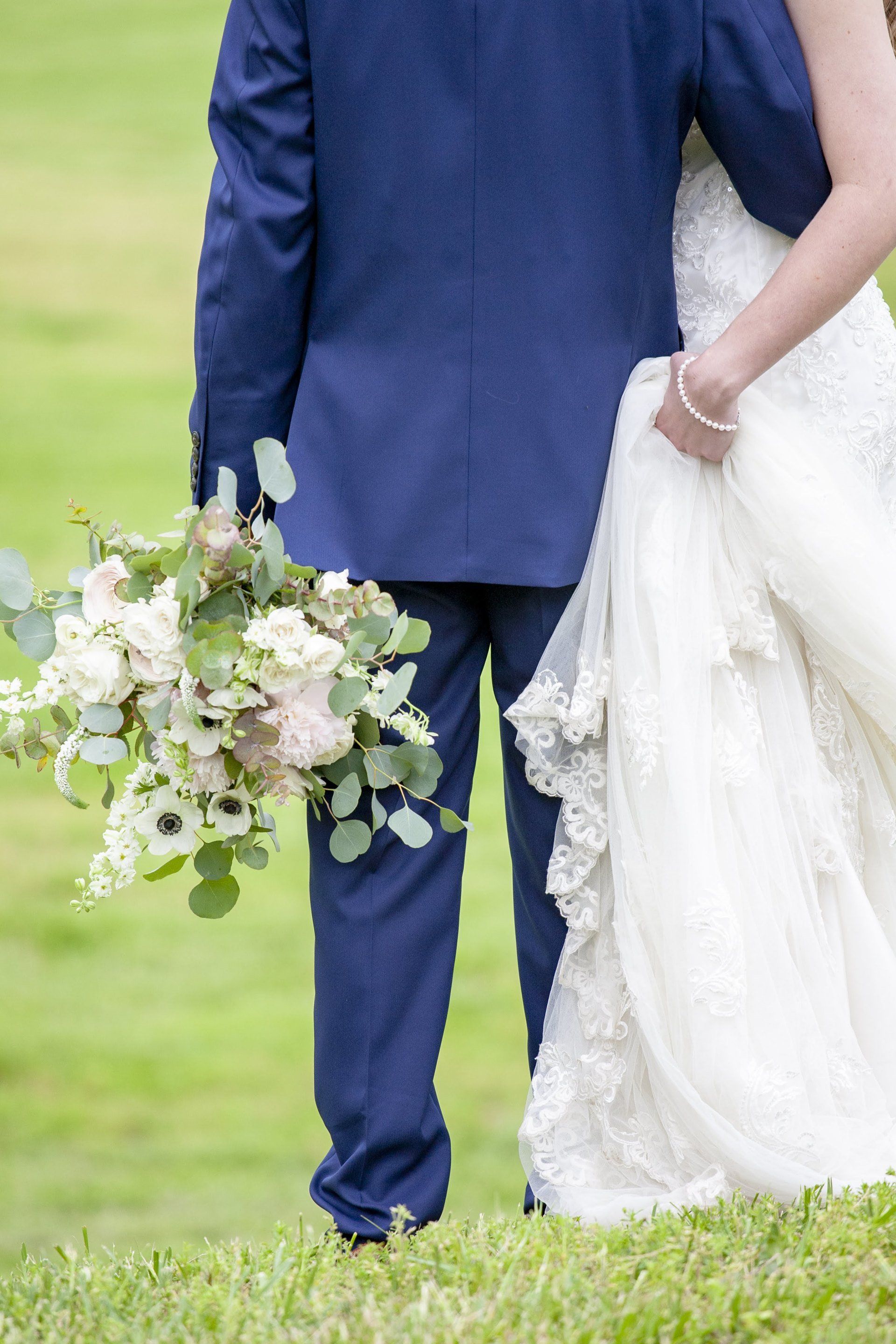 Bride and groom walking on grass, groom holding a bouquet and bride in a white gown