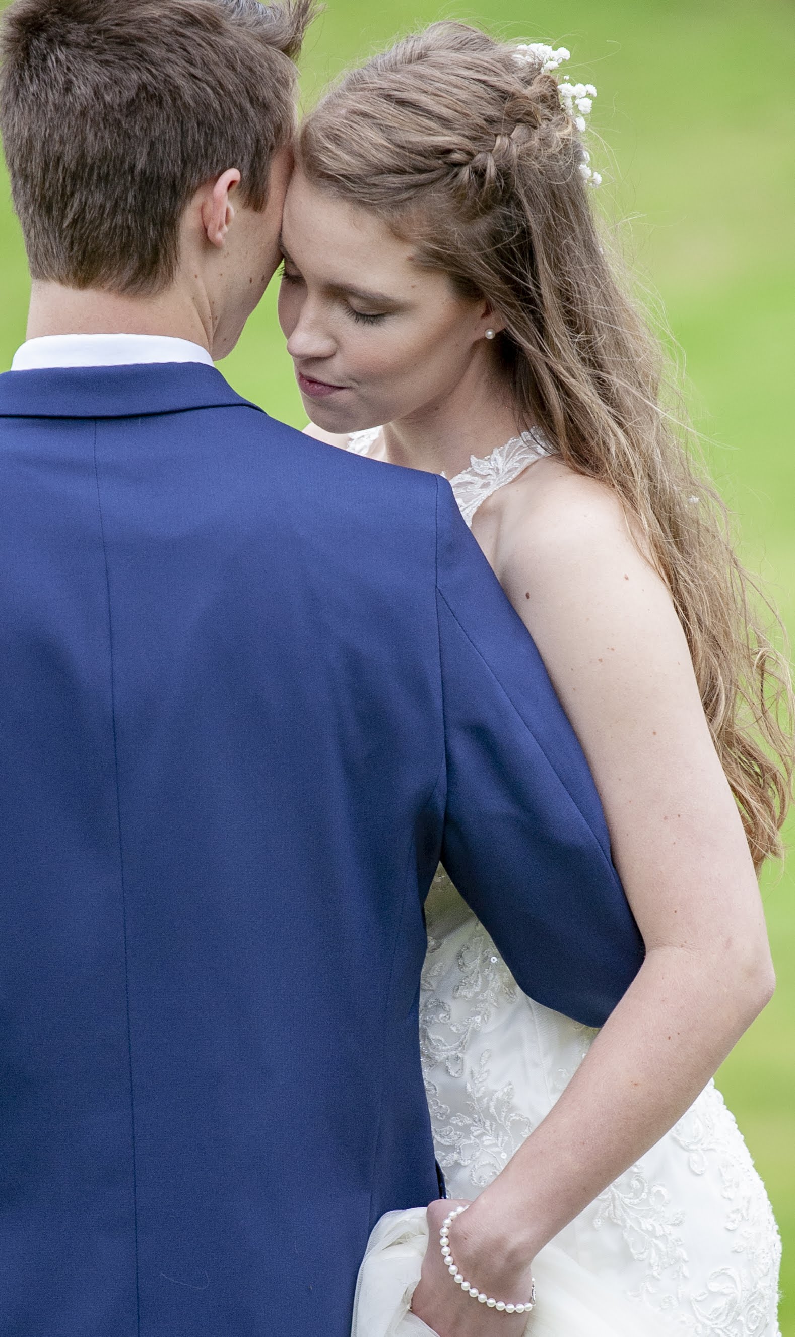Bride and groom embracing outdoors, the bride in a white dress and the groom in a blue suit.