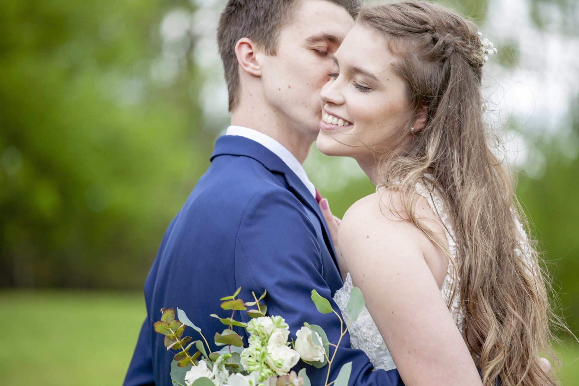 Couple embracing outdoors, with the bride holding a white bouquet.